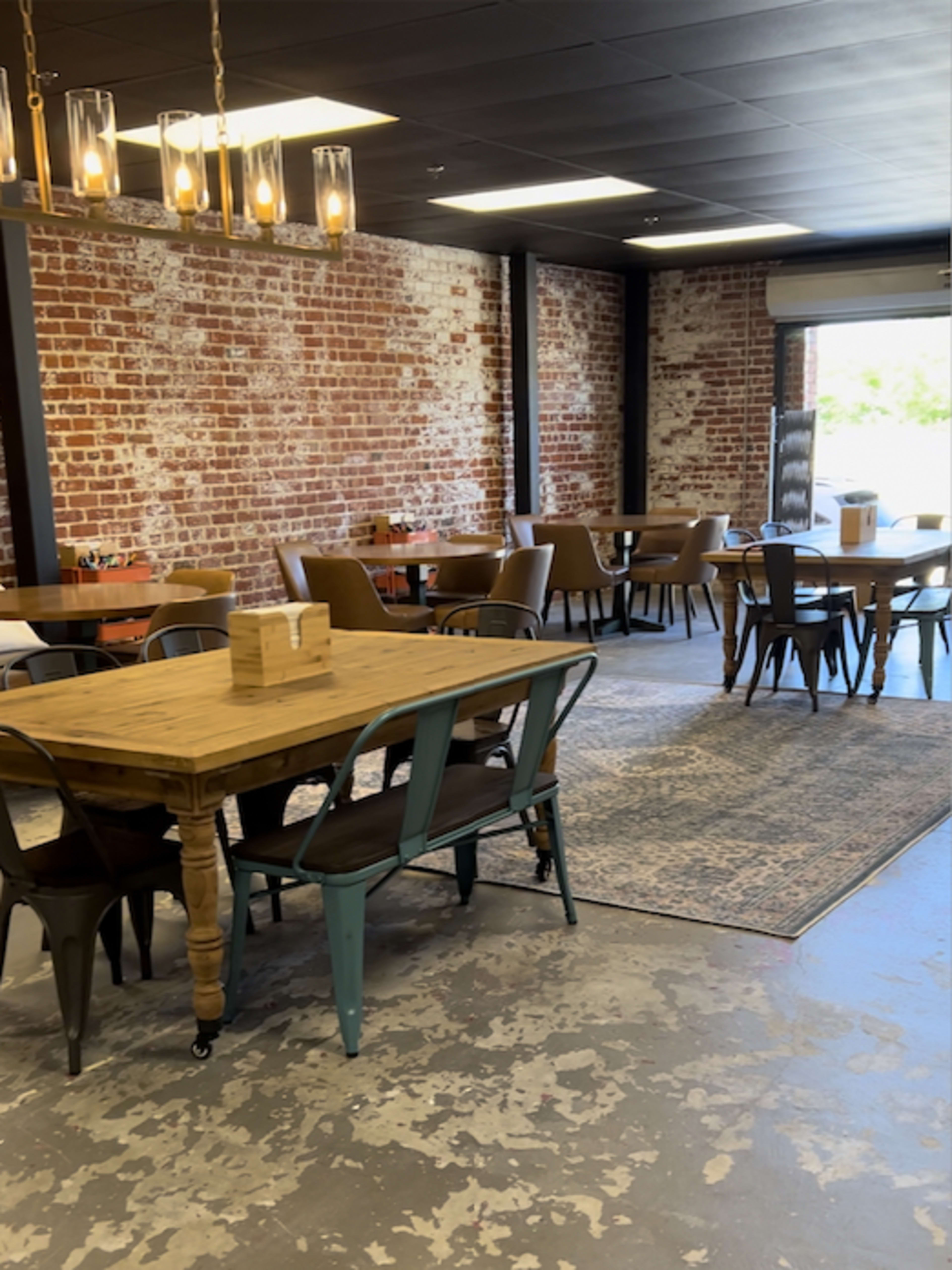 The interior features a spacious room with exposed brick walls, wooden tables, and a mix of metal and upholstered chairs.