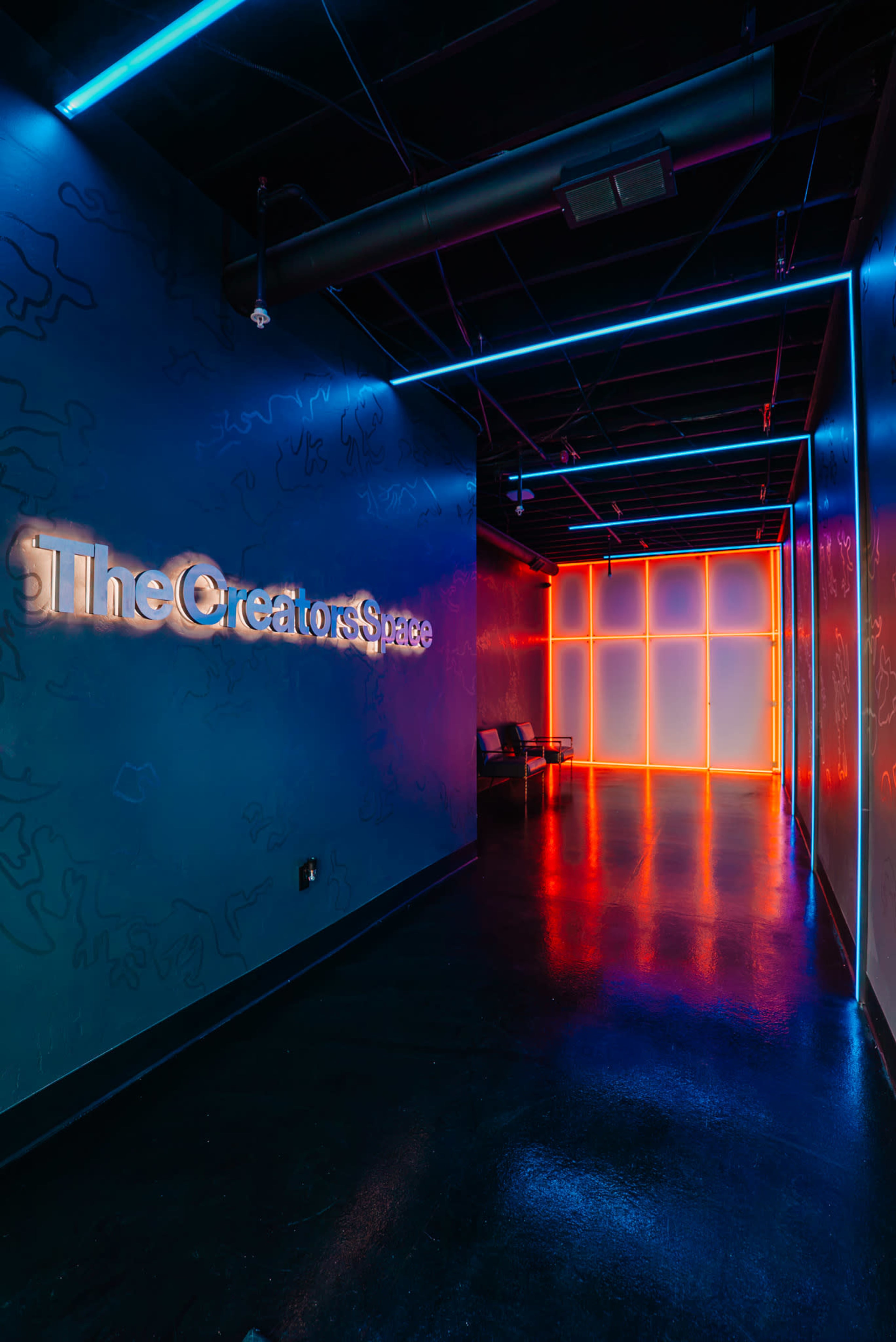 The image shows a modern hallway with a blue and black color scheme, illuminated by neon blue and orange lights, leading to a brightly lit area marked with the text "TheCreatorsSpace."