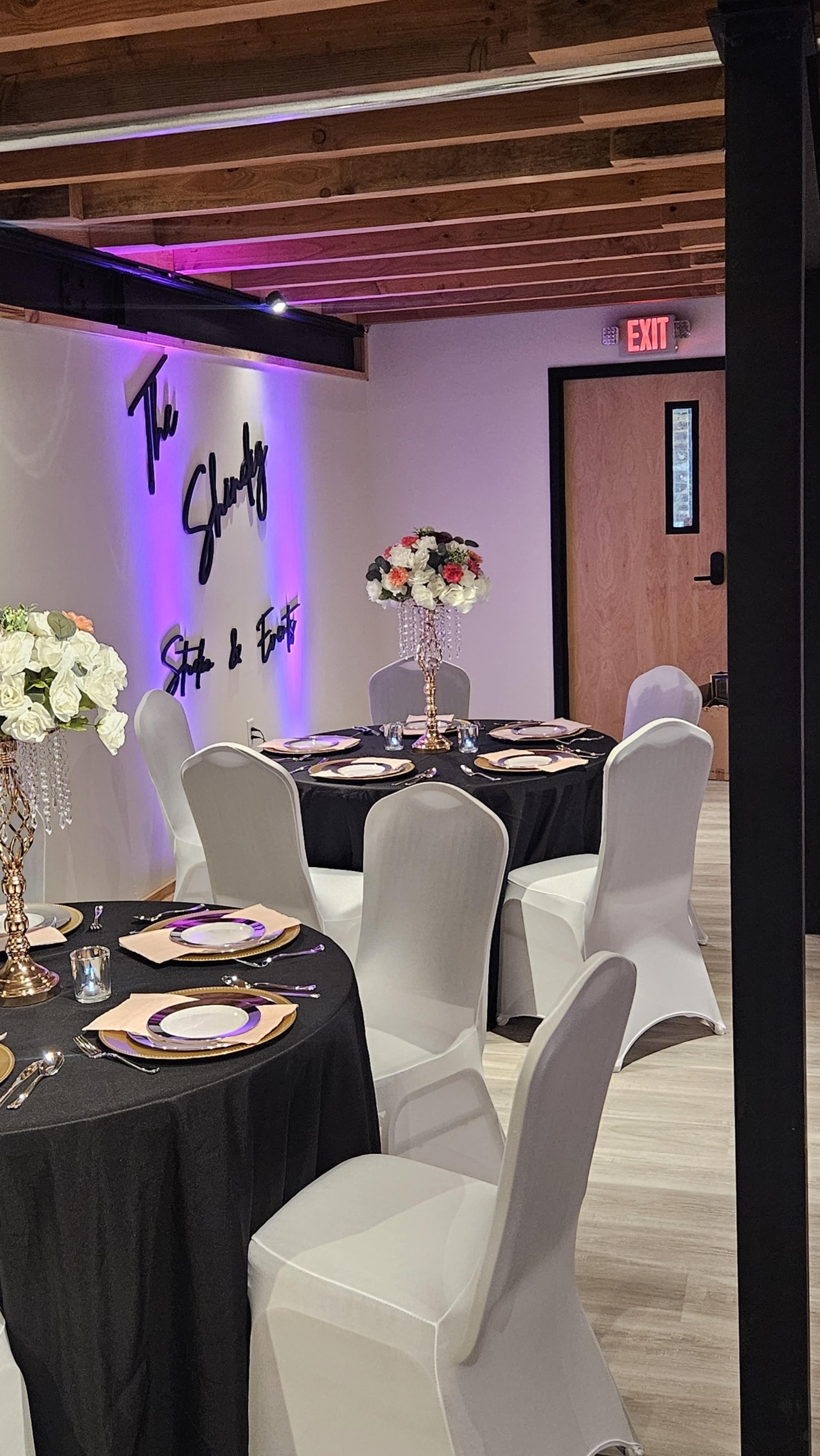 A decorated banquet room with black tablecloths, elegant centerpieces, and purple lighting.