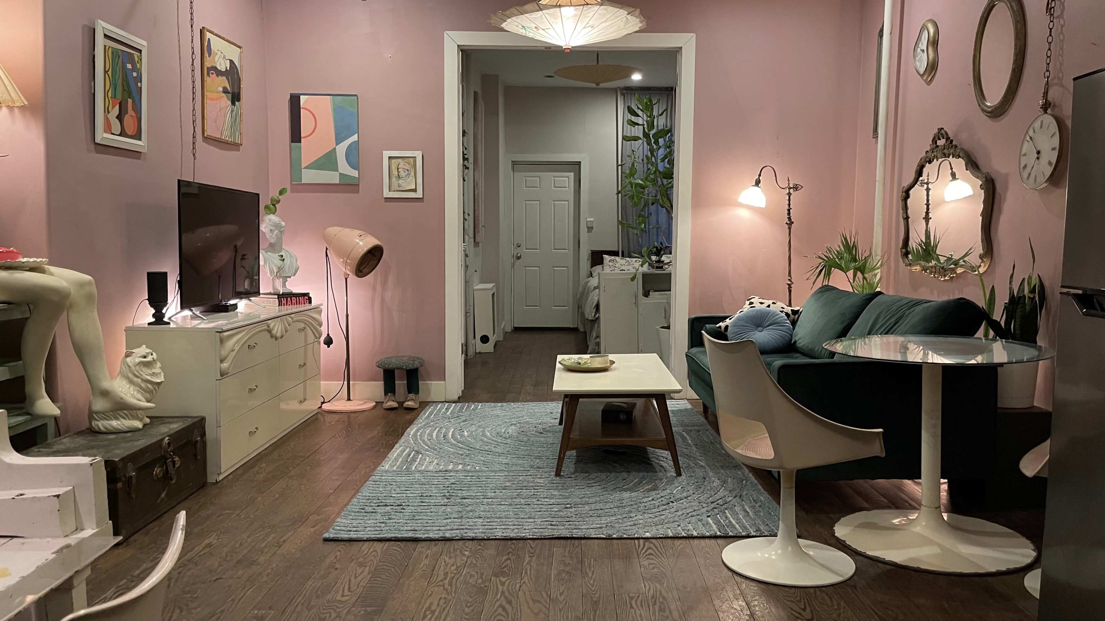 The image shows a cozy living space with pink walls, a green sofa, a round dining table, and a combination of modern and vintage decor.