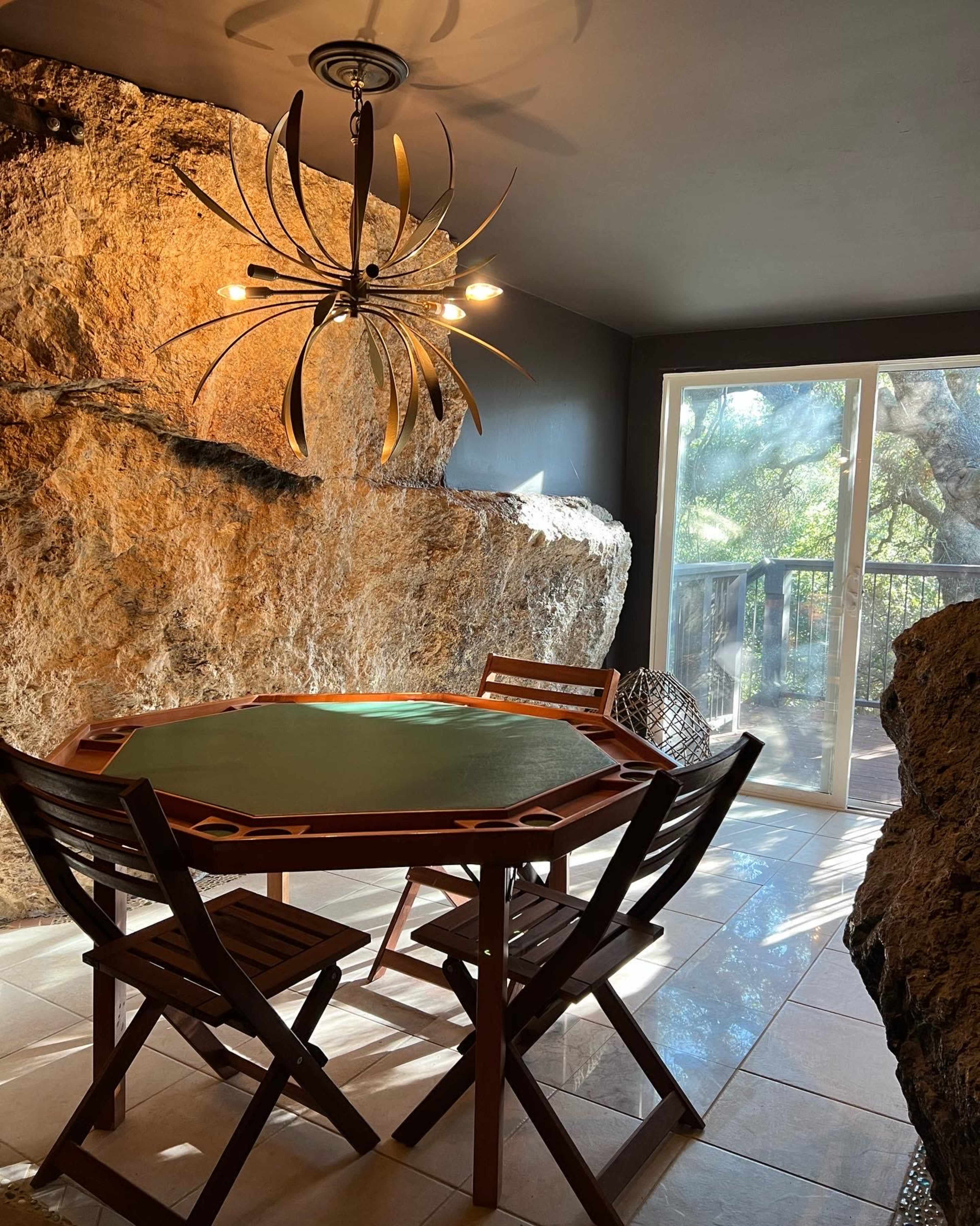 A wooden table with four chairs is positioned in a room featuring a rock wall and a pendant light fixture.