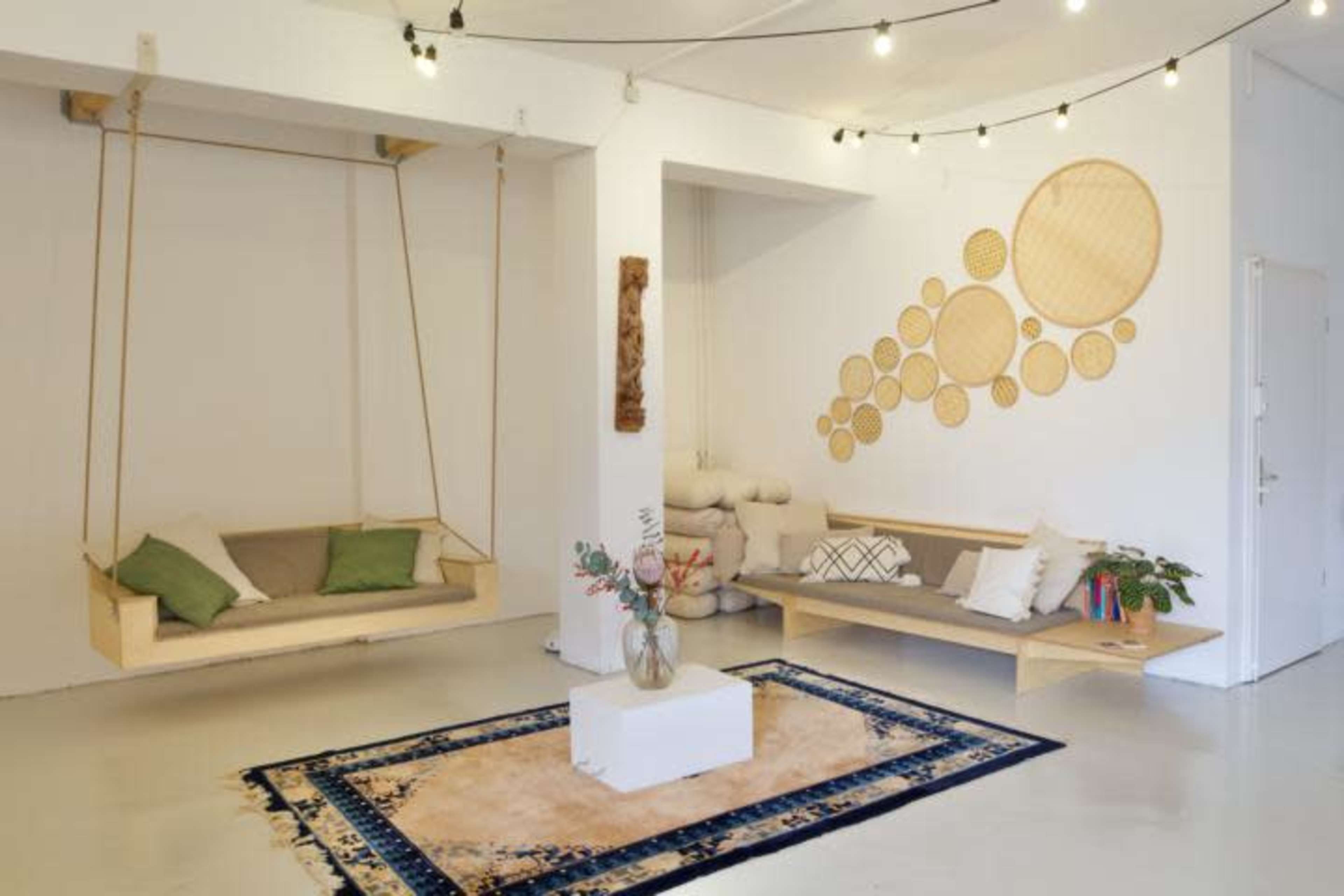 A minimalist living space featuring a wooden swing, a low wooden bench, a patterned rug, and decorative wall art made of circular wooden elements.