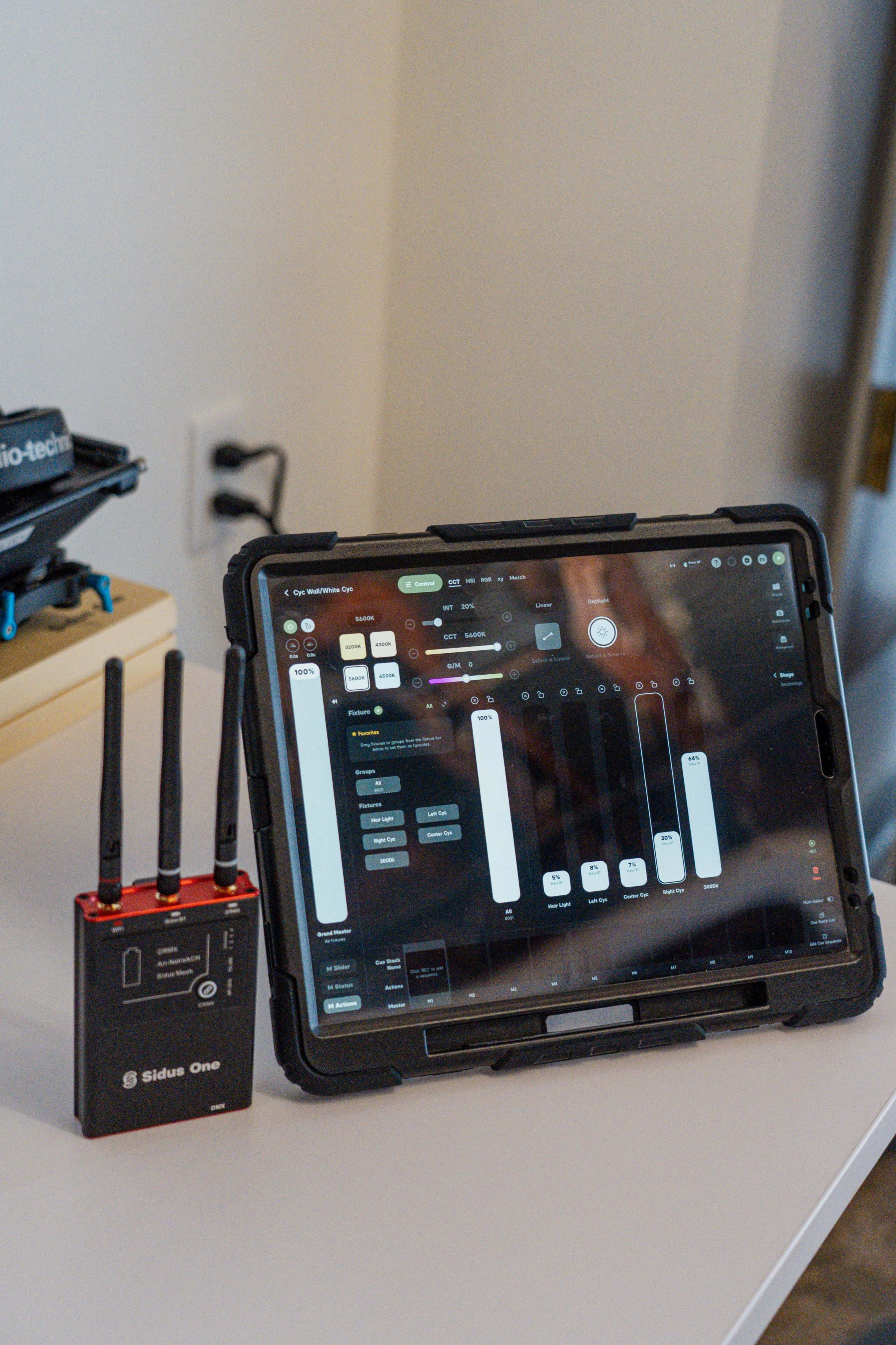 A tablet displaying a control interface is positioned next to a Sidus One wireless control device with three antennas on a table.