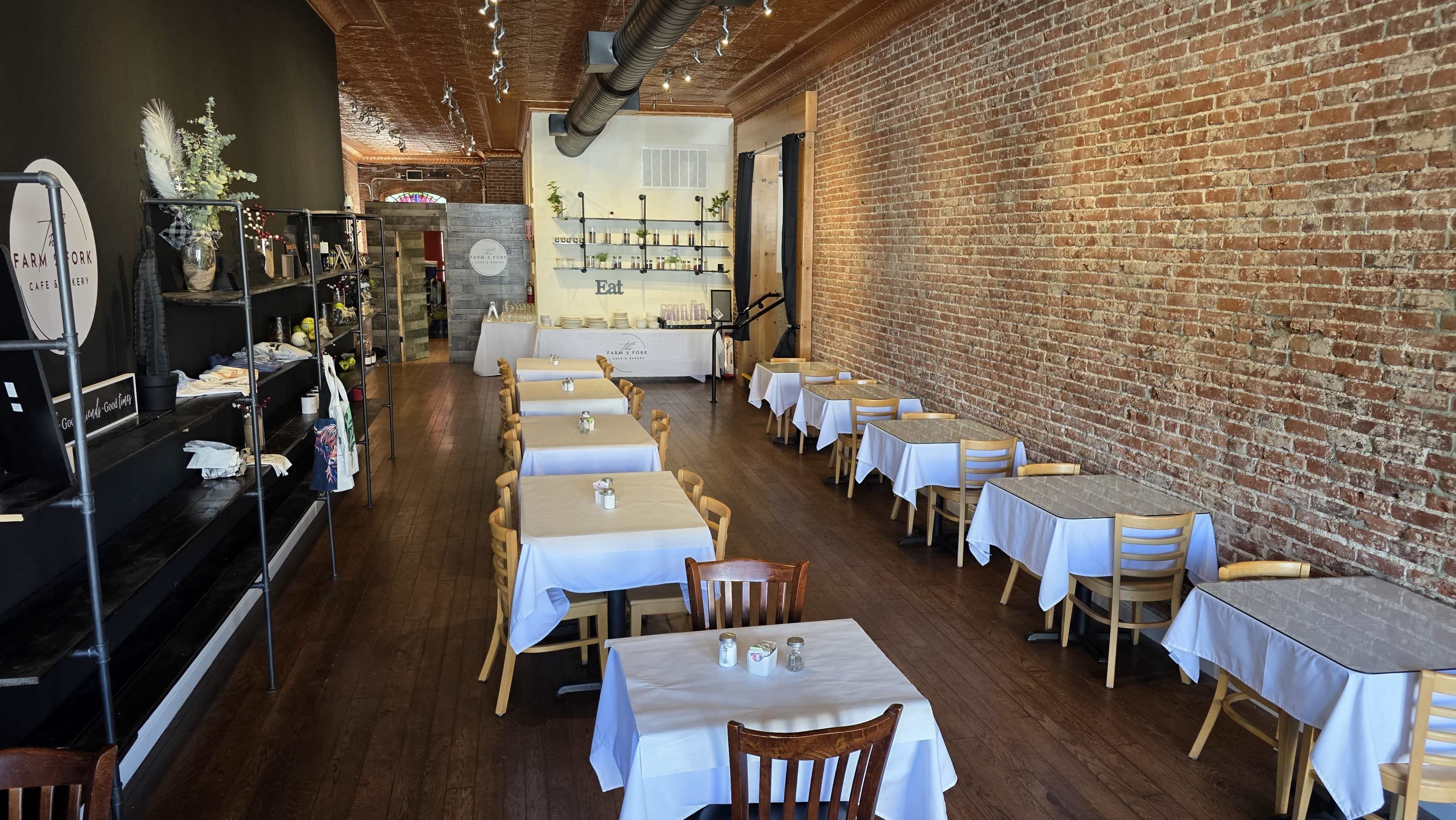 The image shows a spacious restaurant with wooden flooring, exposed brick walls, and tables set with white tablecloths.