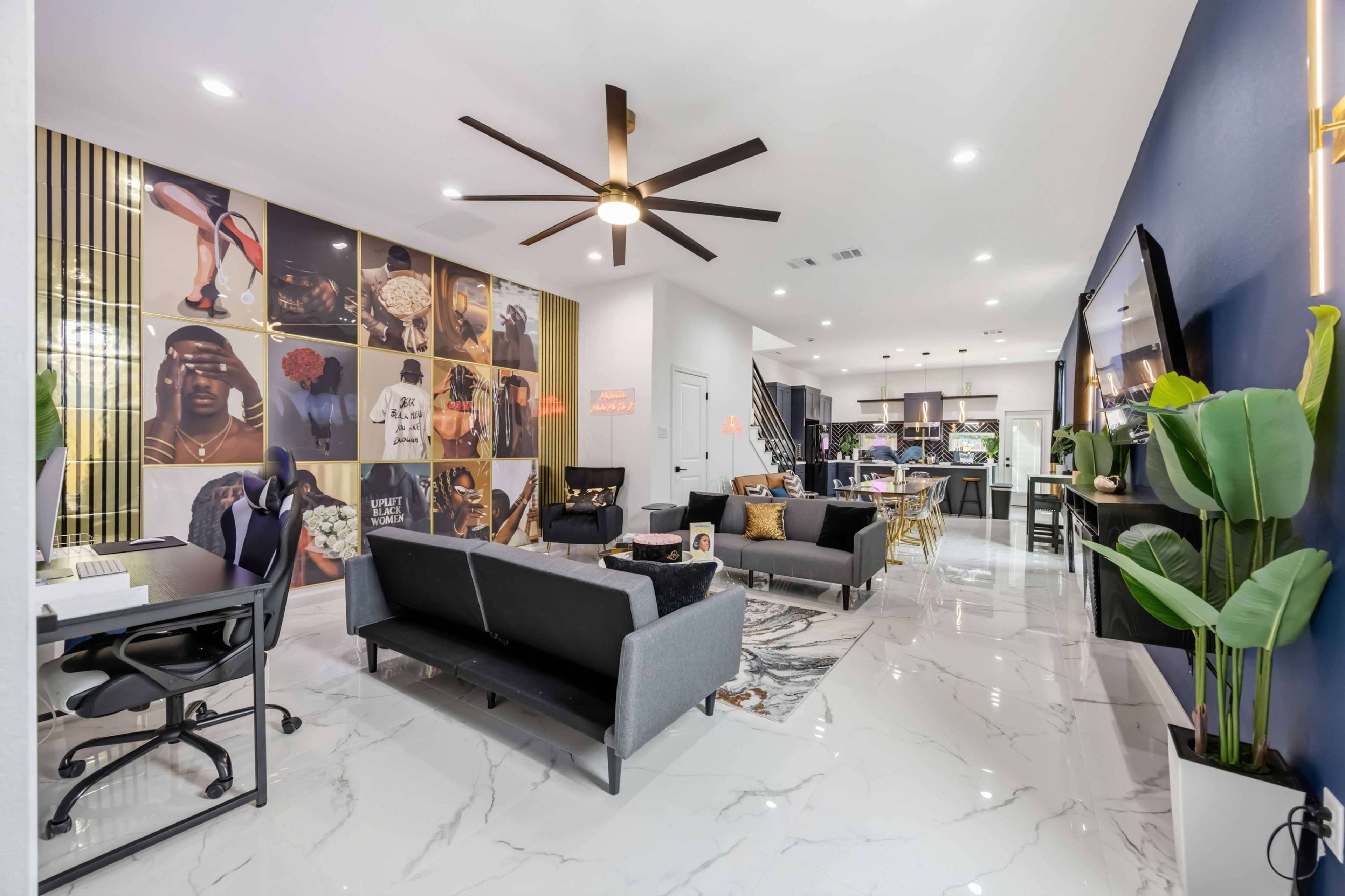 The image shows a modern open-concept living space featuring a stylish living room with a large wall adorned with framed art, a dining area, and a kitchen visible in the background.