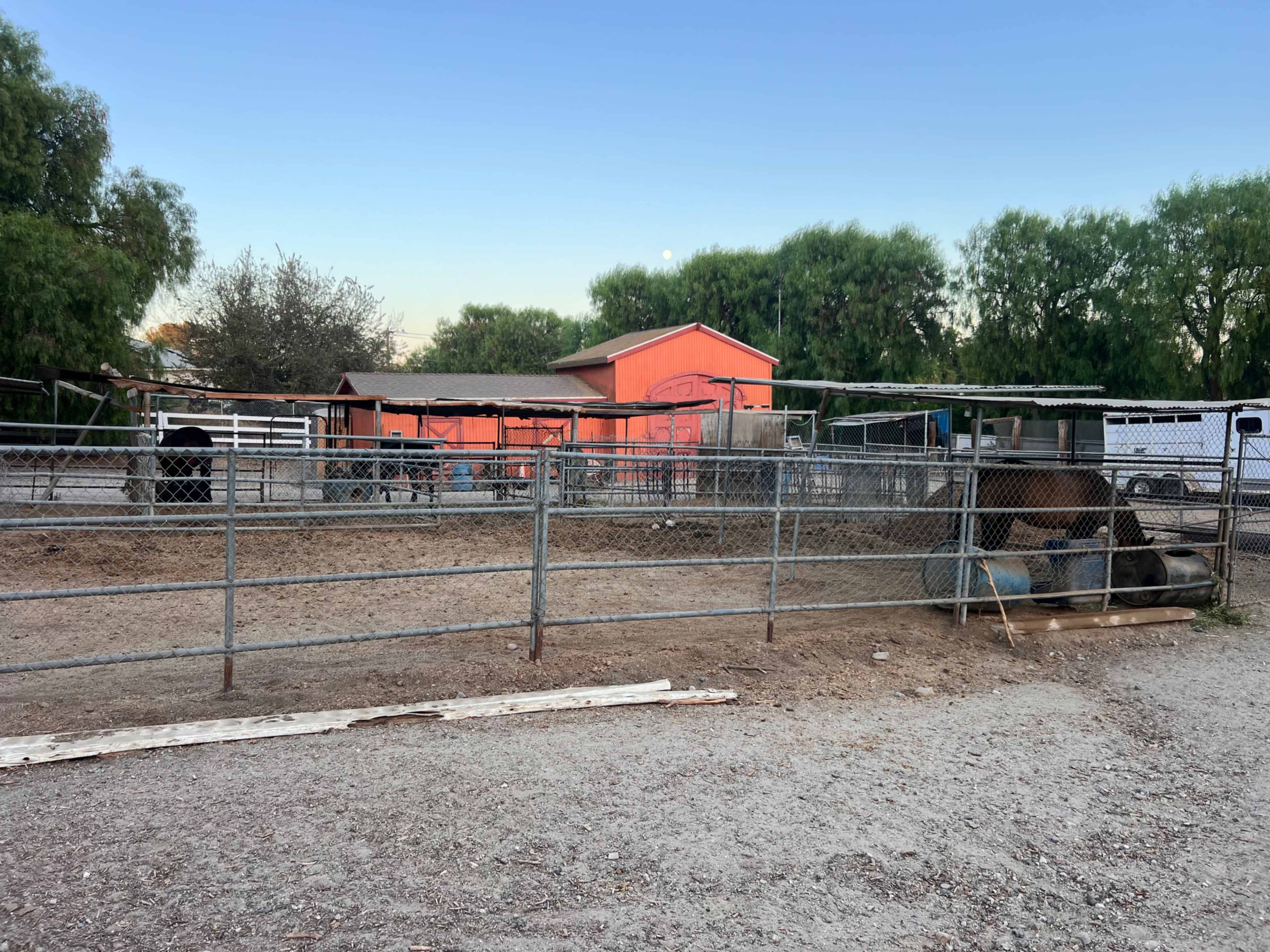 The image shows a fenced enclosure at a ranch with multiple horse stalls and a pink building in the background.