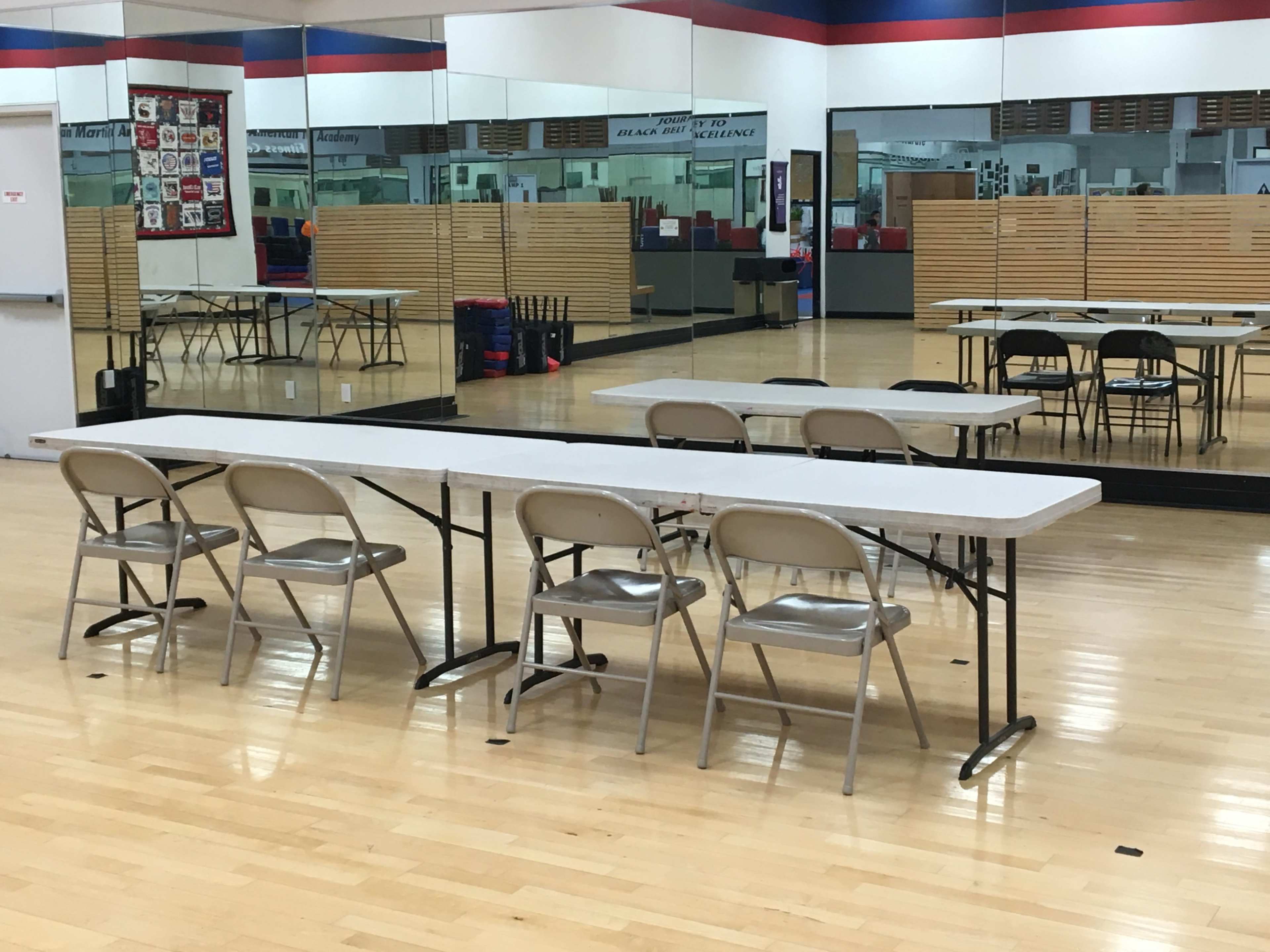 A long table with several chairs is set up in a mirrored room with wooden floors.