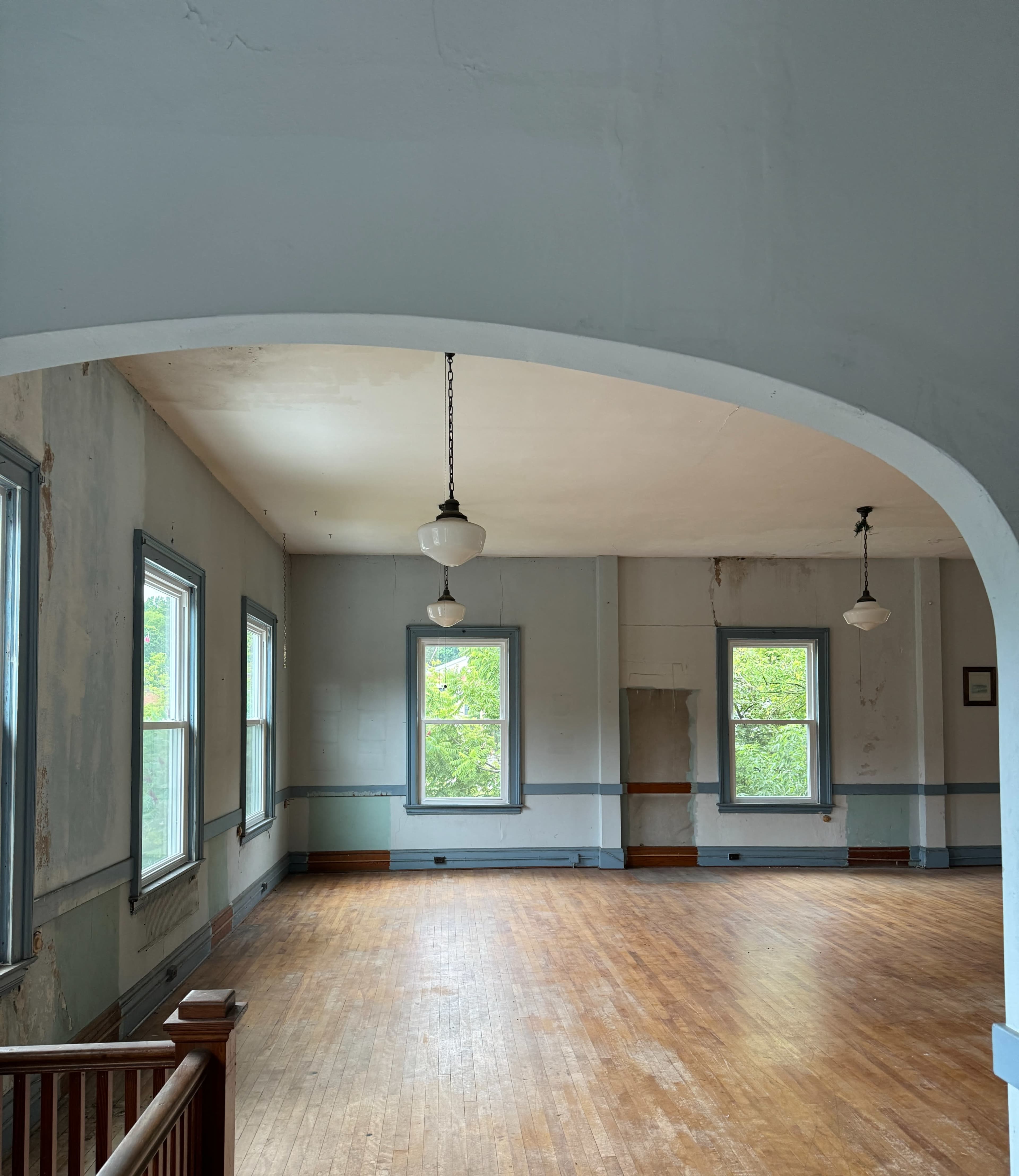 An empty, well-lit room with wooden floors, large windows, and a curved archway with hanging lights.