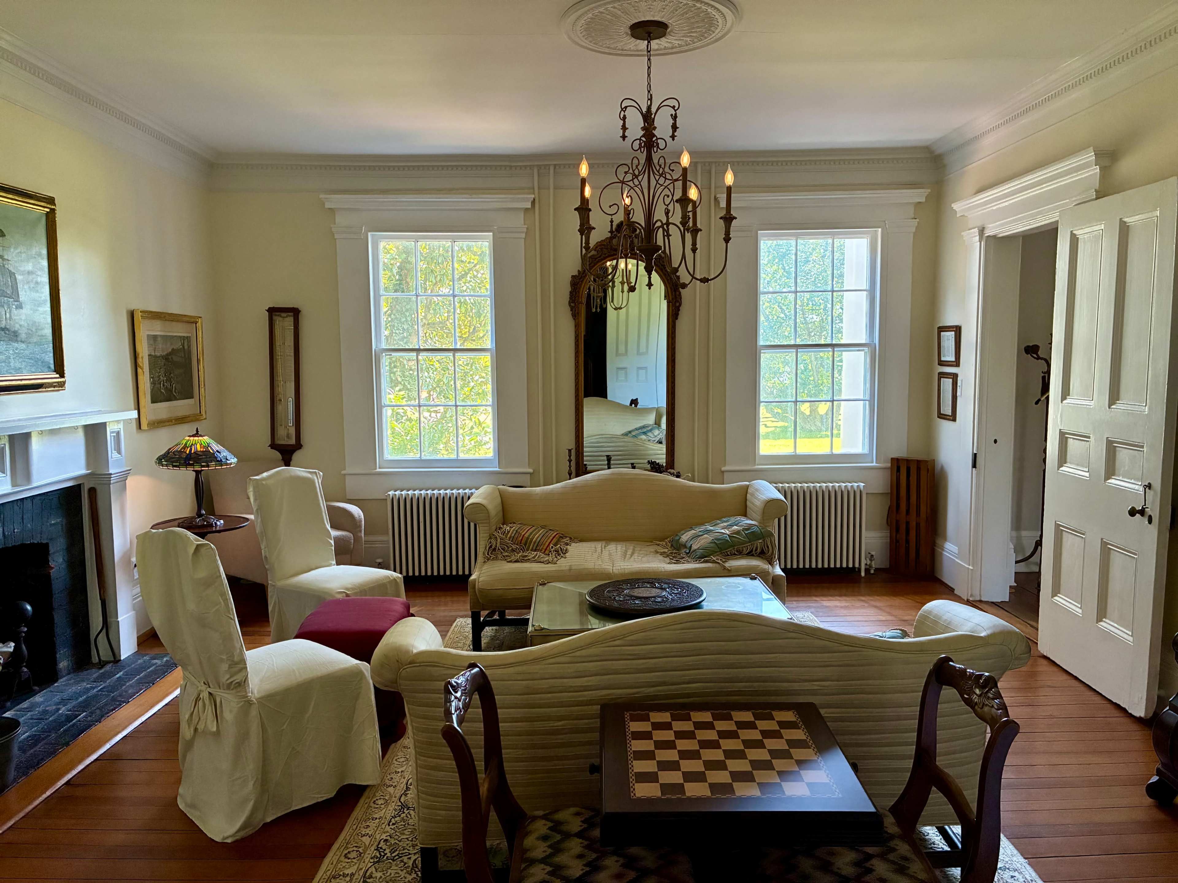 The image shows a spacious living room with a chandelier, a chessboard table, and several comfortable seating arrangements.