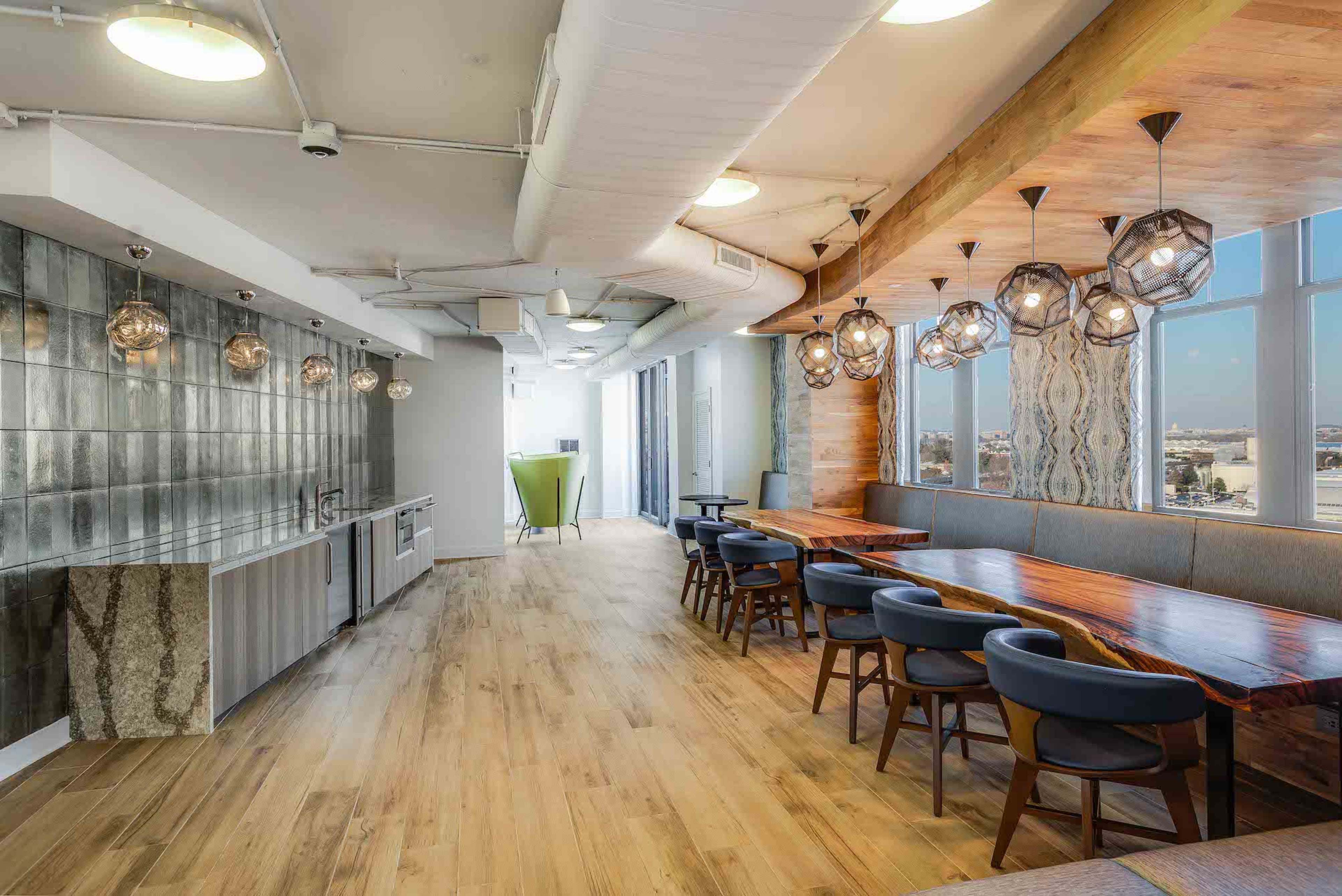 A modern dining area with a large wooden table, stylish chairs, and decorative light fixtures, situated in a bright room with large windows.