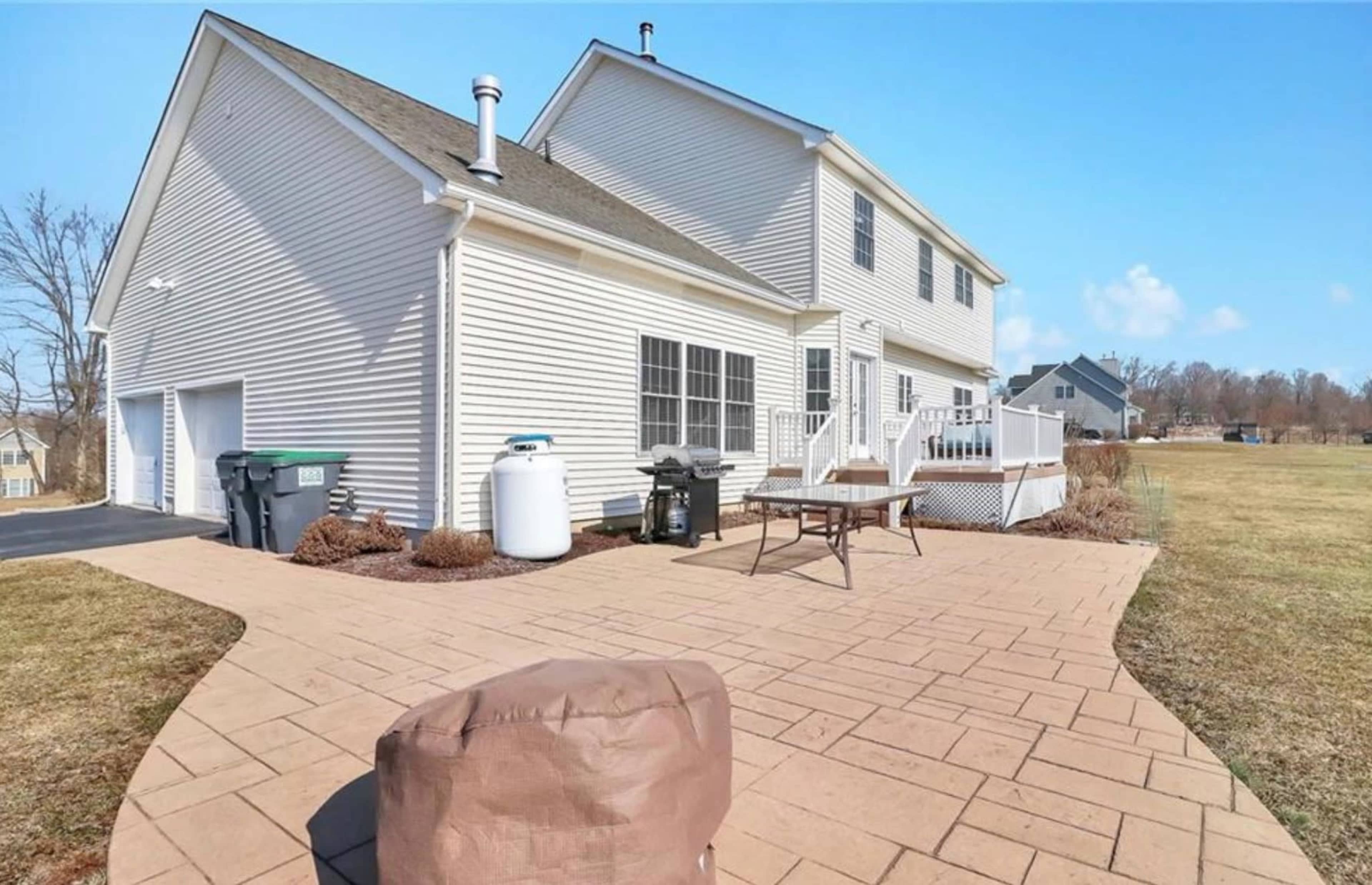 The rear exterior of a two-story house with a patio, green lawn, and outdoor furniture.