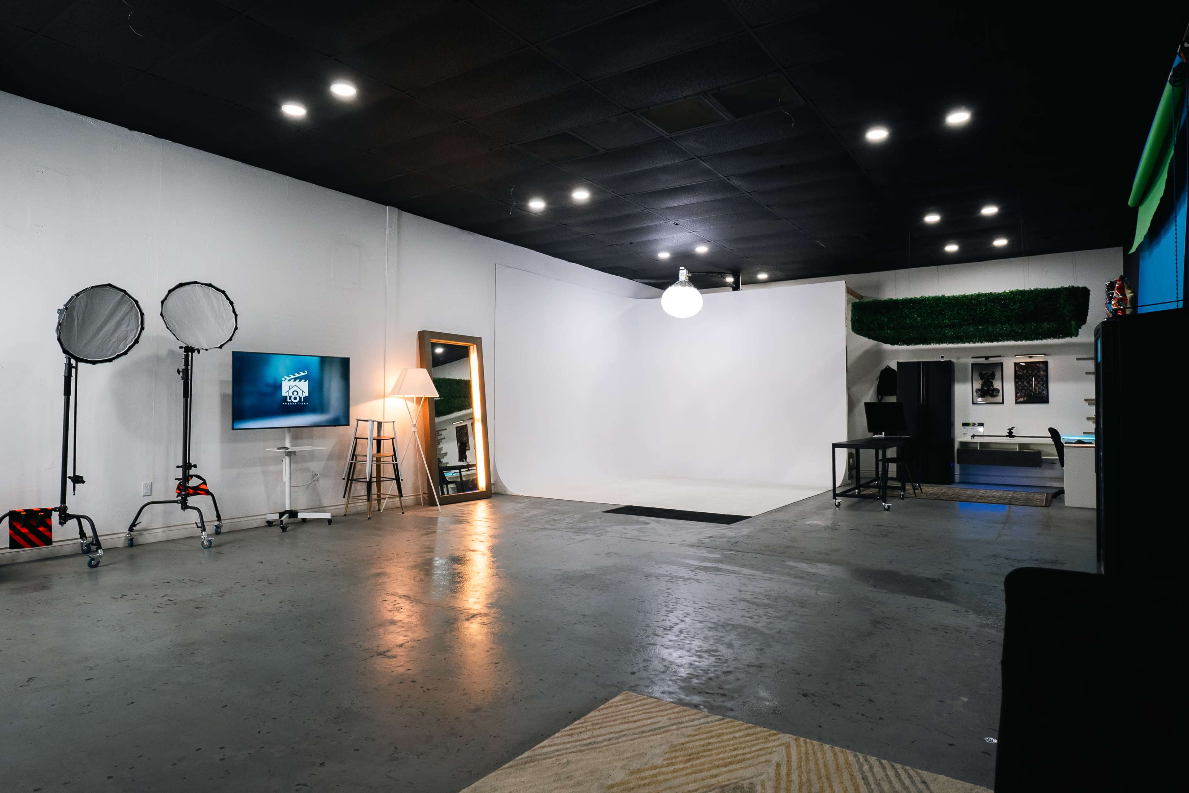 A spacious studio with a blank white backdrop, equipped with lighting stands, a television on a stand, and various furniture pieces.