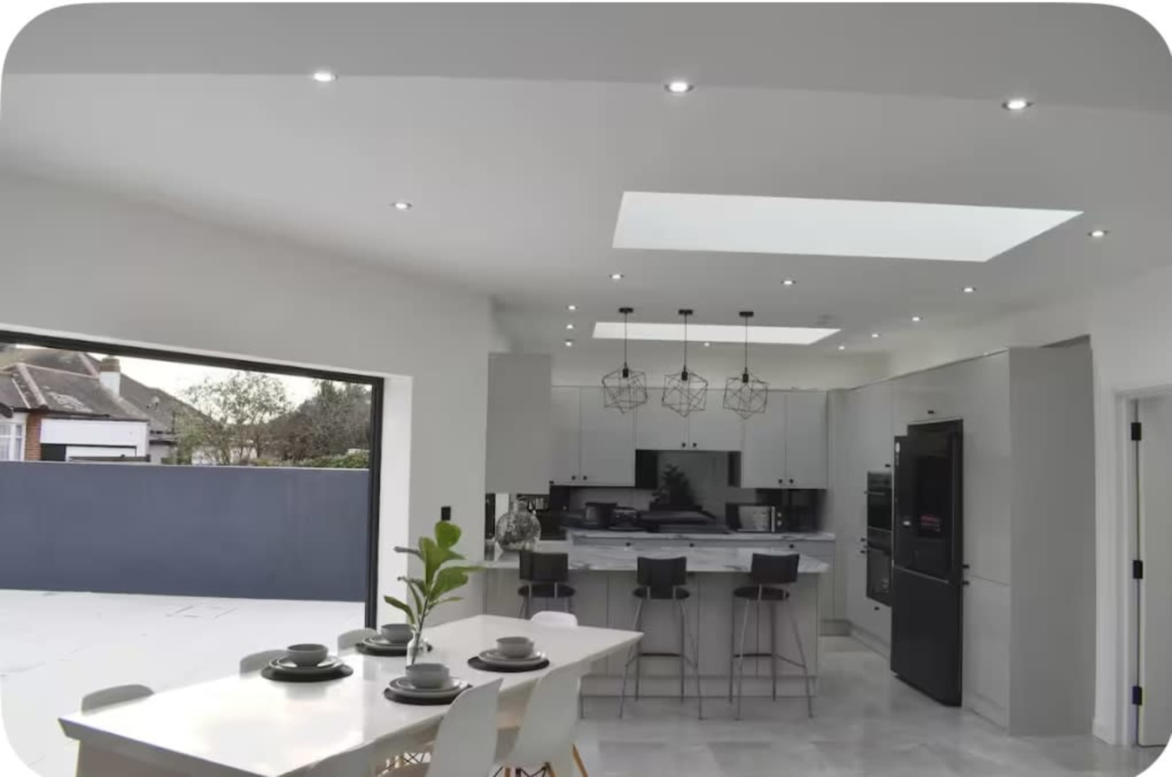 A modern kitchen features a central dining table, sleek cabinetry, and large windows that provide natural light.