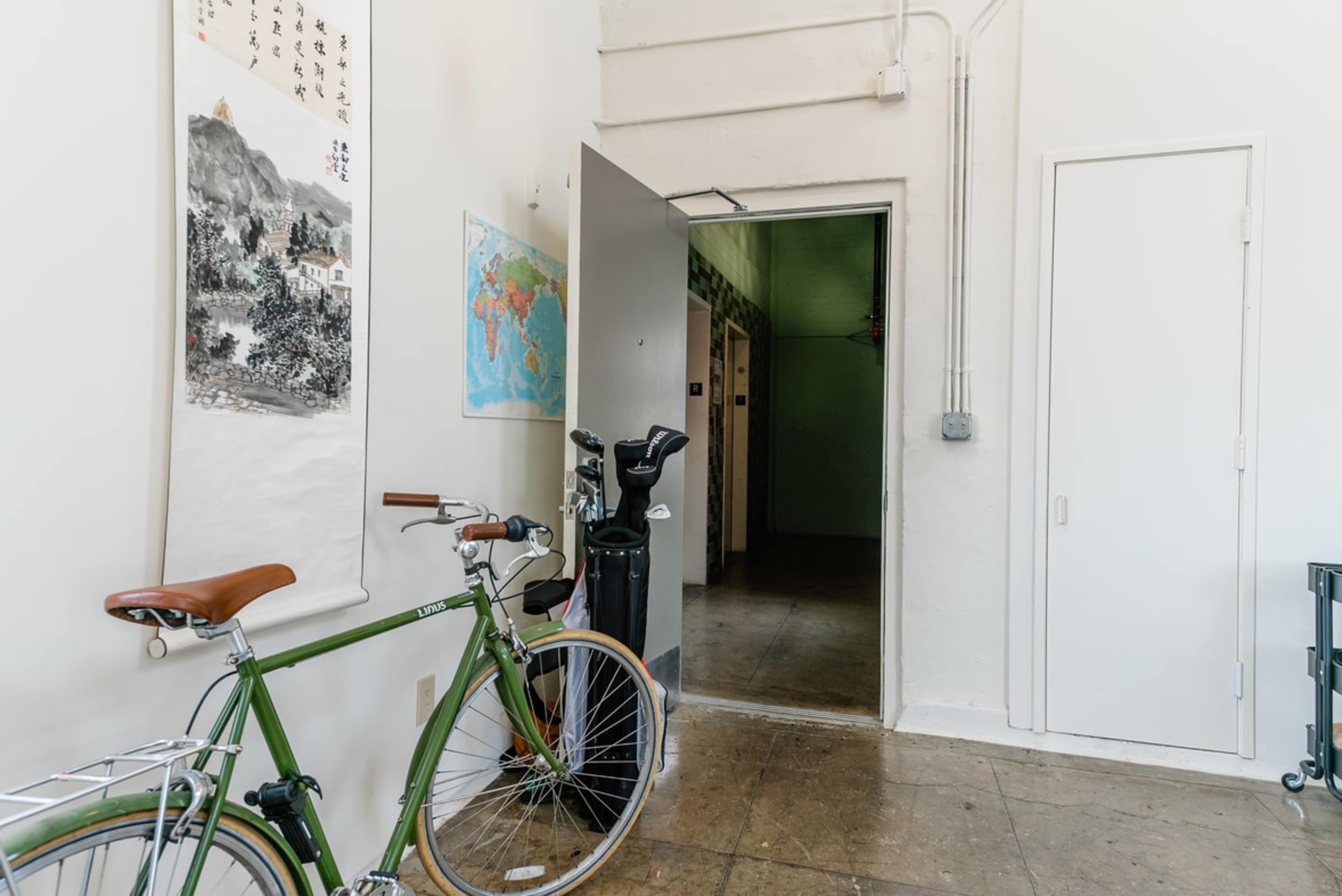 A hallway with a green bicycle parked against a wall, a golf bag, and a door leading to another room, along with maps and artwork on the walls.