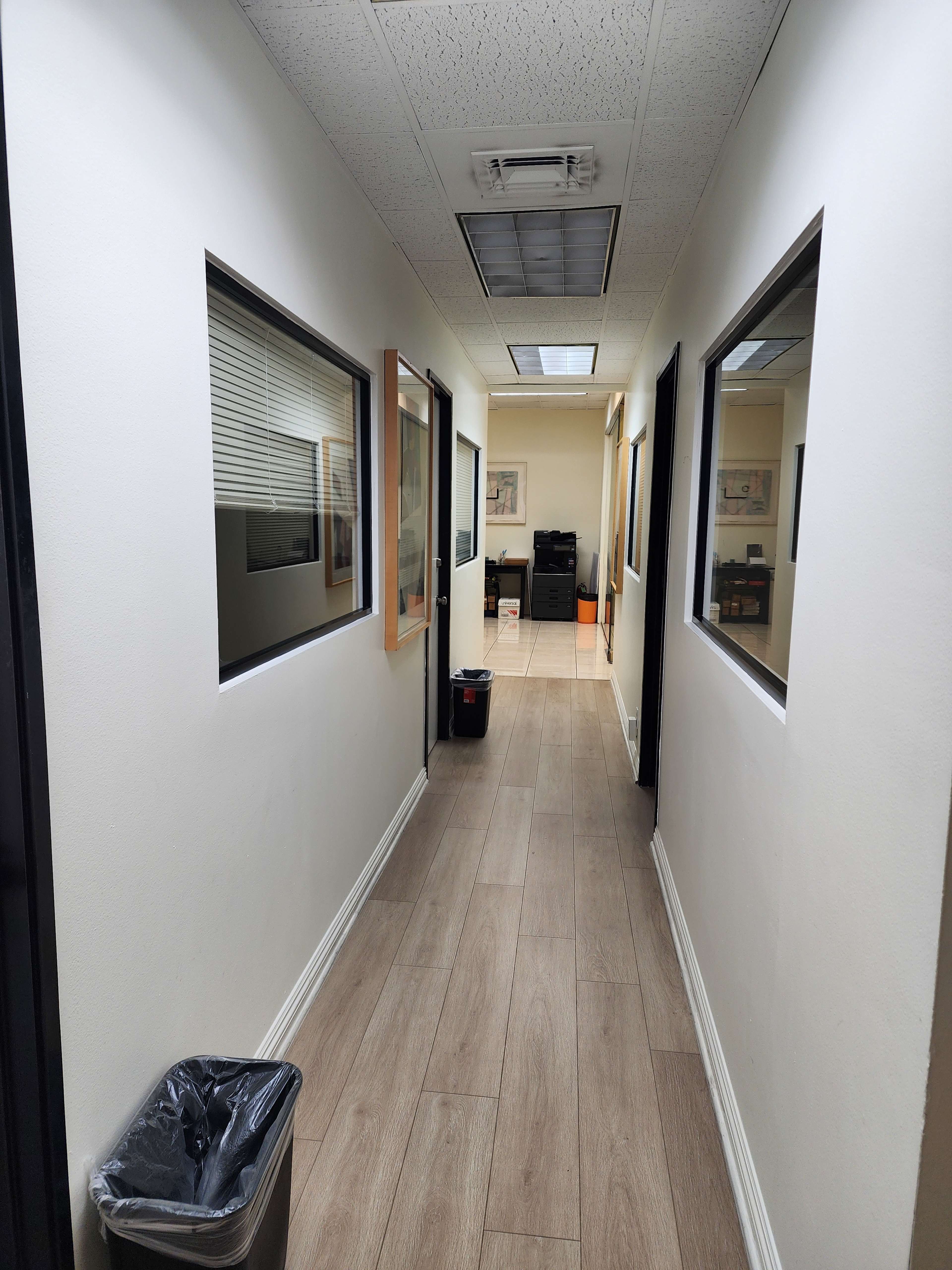 The image shows a narrow hallway with several windows along the walls, leading to an office space at the end.
