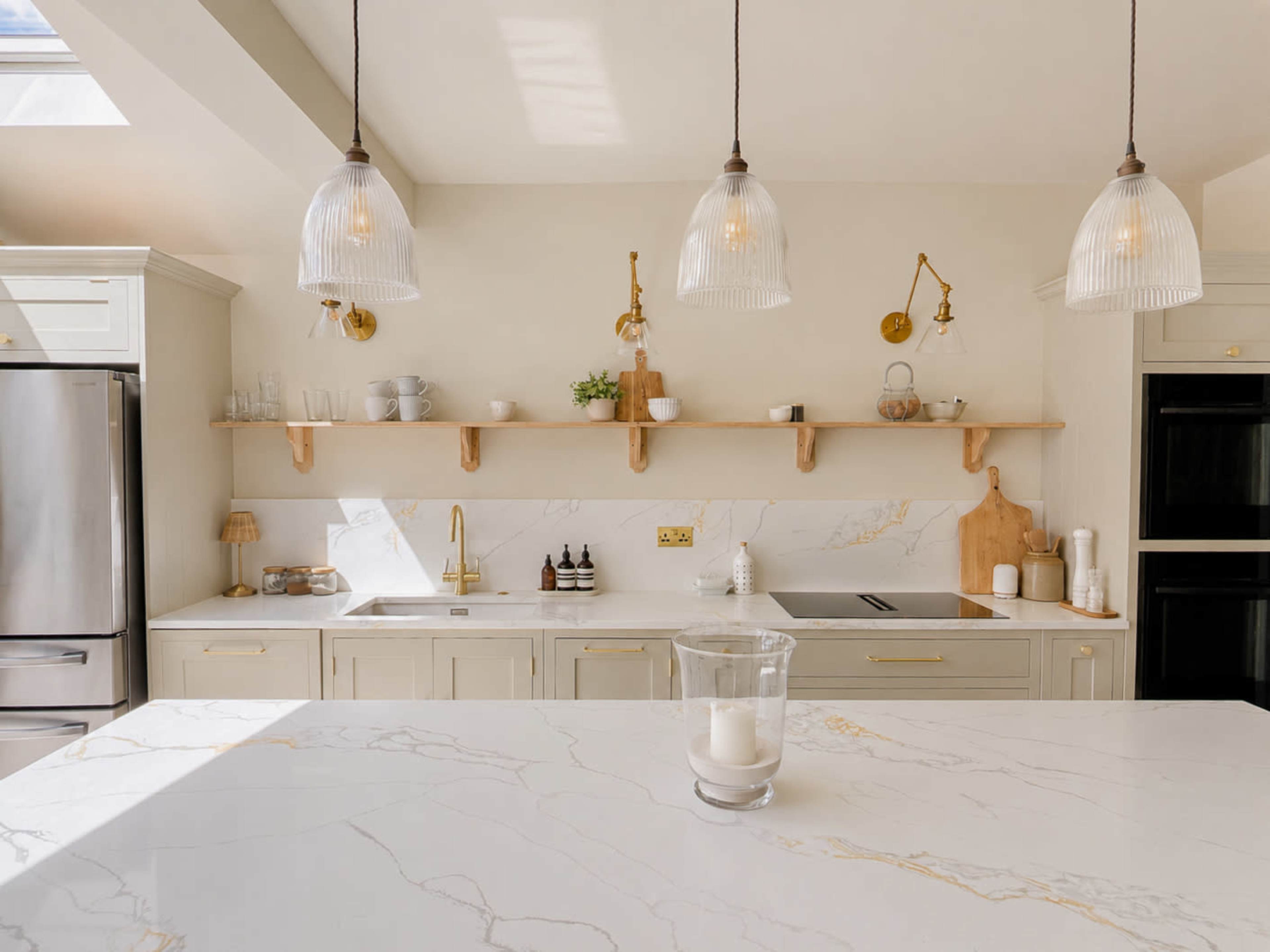 A modern kitchen features a spacious countertop, marble surfaces, pendant lighting, and open shelving with decorative items.