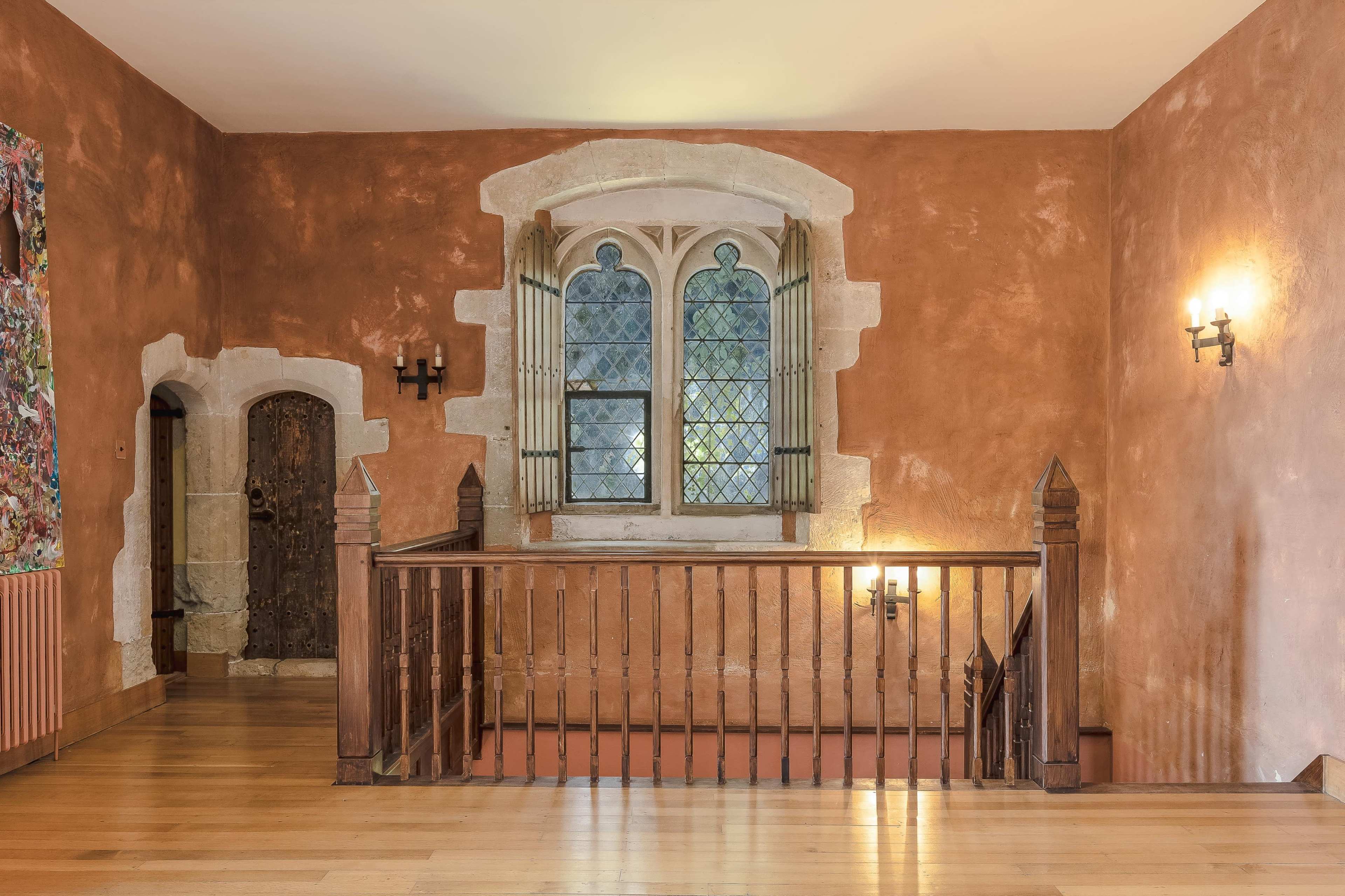 A hallway with a wooden railing, an arched window featuring leaded glass, and walls finished in a warm, earthy color.