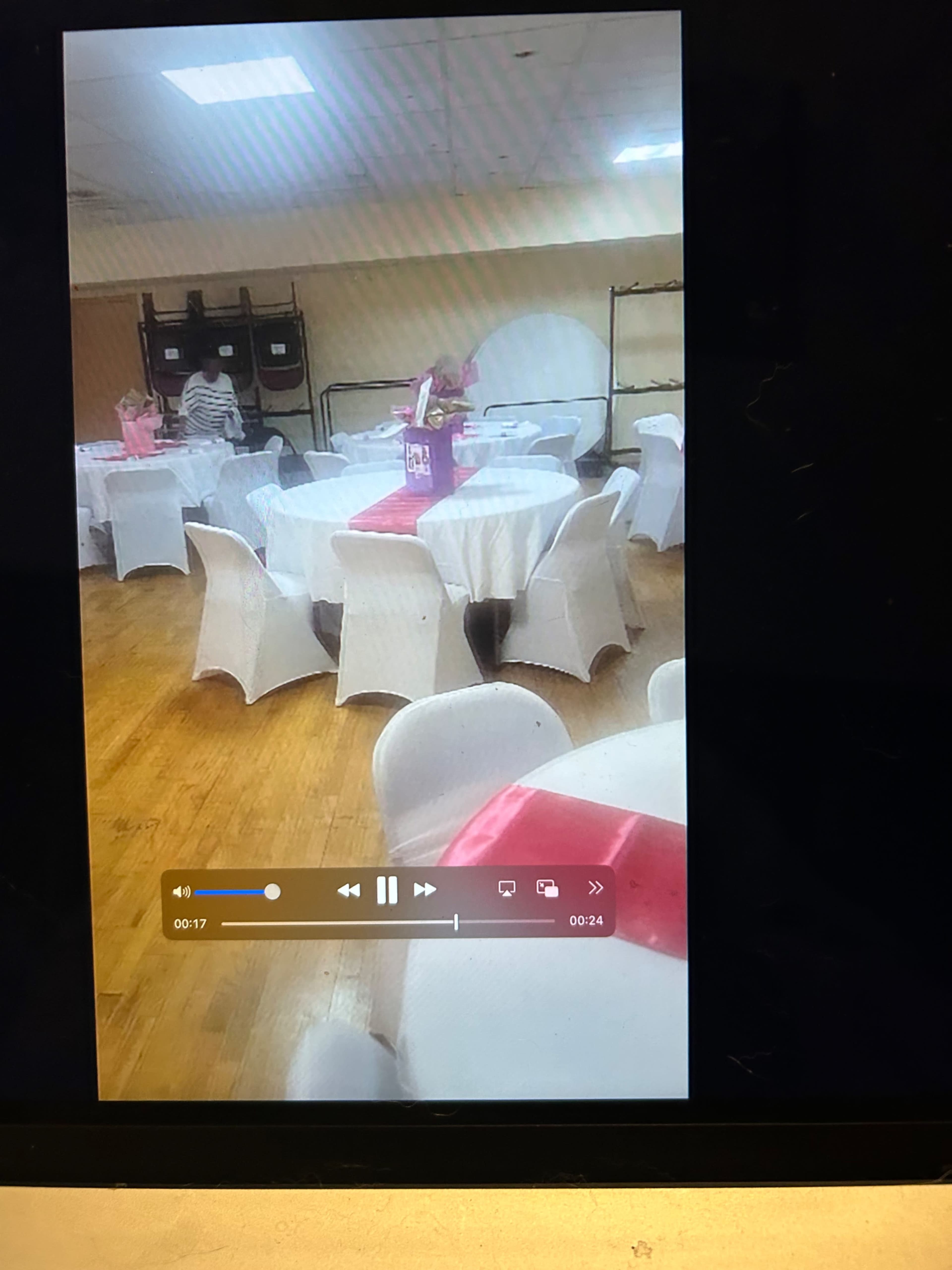 A spacious banquet room features several round tables covered with white tablecloths and pink accents.