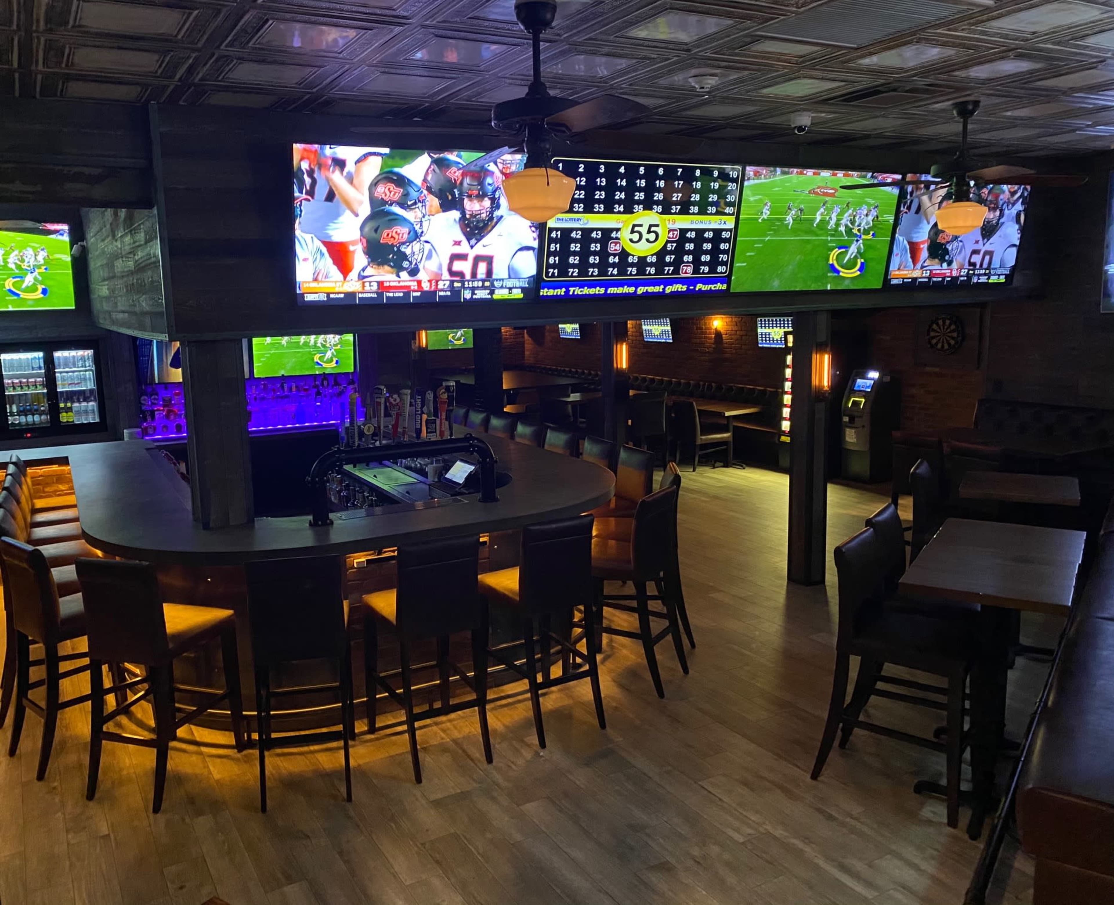 A sports bar with multiple flat-screen televisions displaying games, a central circular bar with seating, and wooden tables arranged around the room.