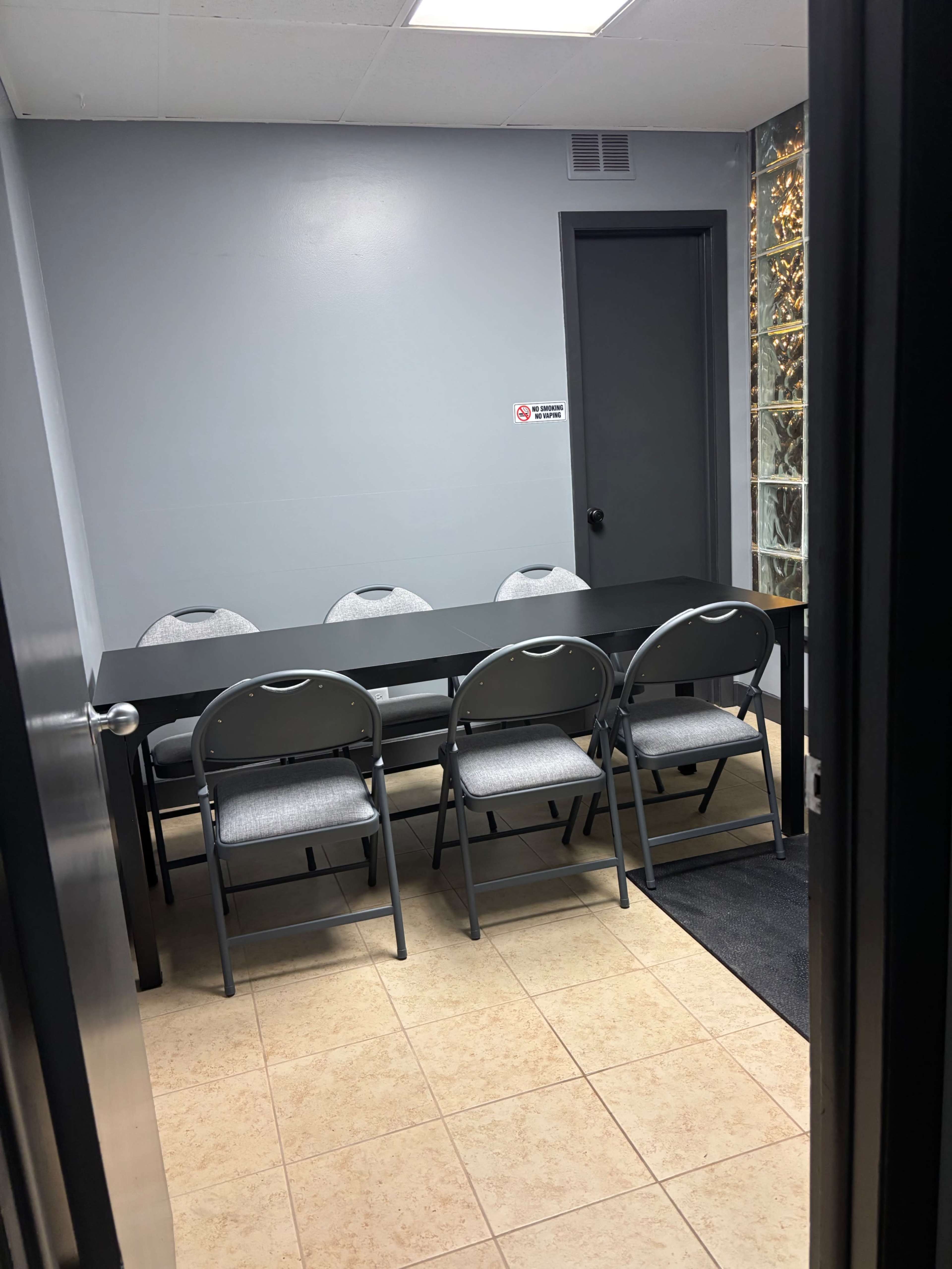 The image shows a small meeting room with a rectangular table and four chairs arranged neatly around it.