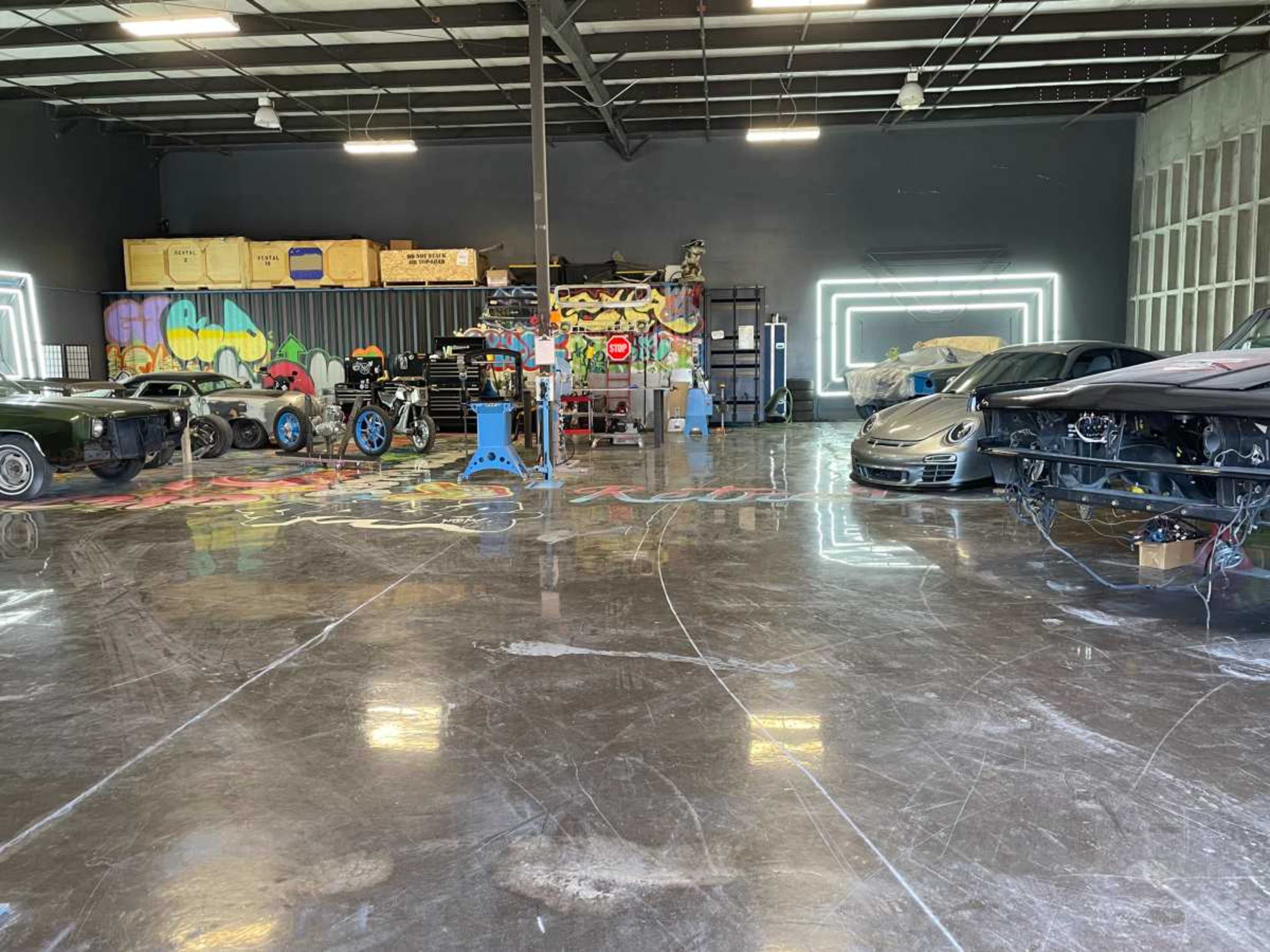 The image shows a spacious garage with several cars, tools, and colorful graffiti on the walls.