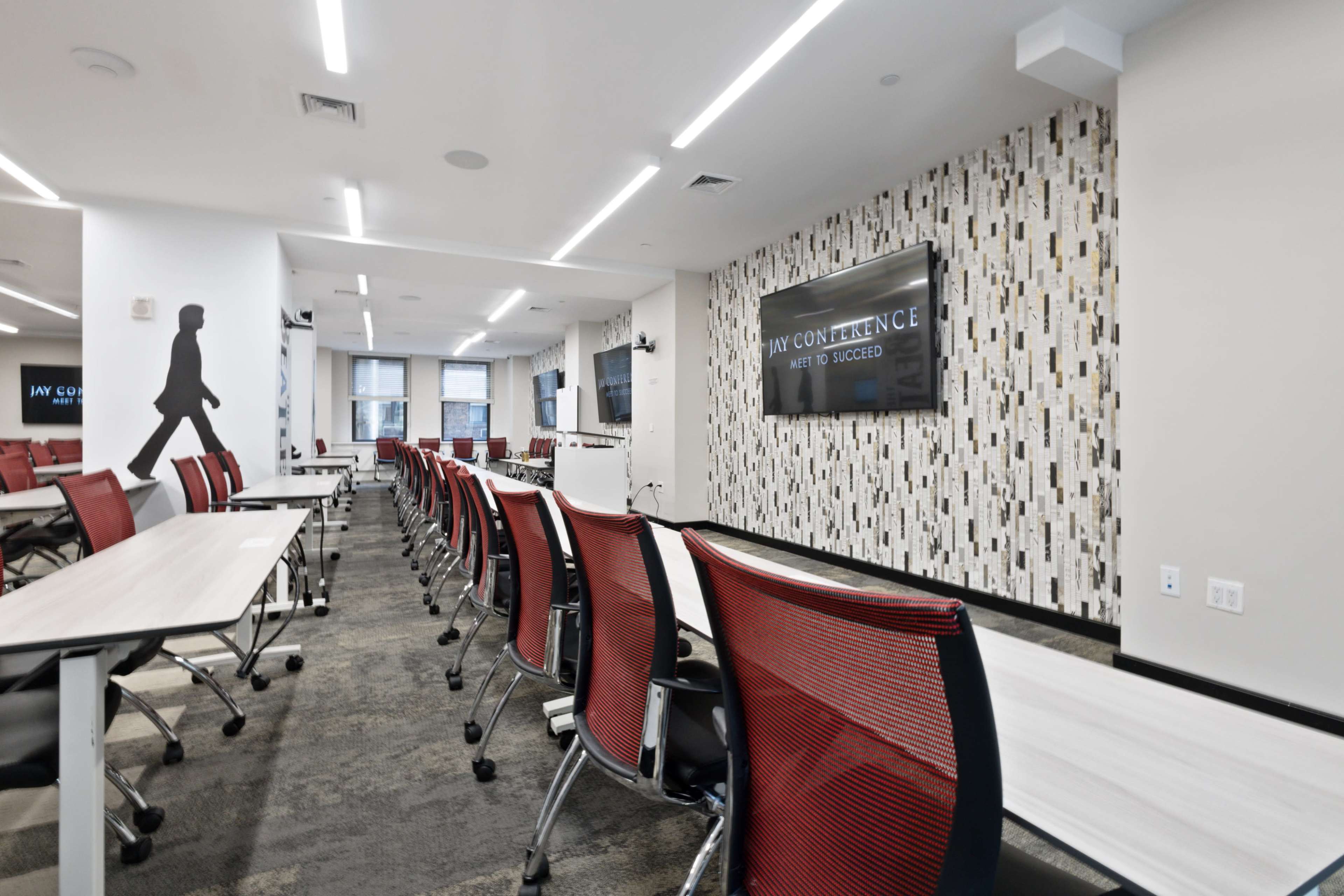A modern conference room with rows of red chairs facing a projection screen and a decorative wall.
