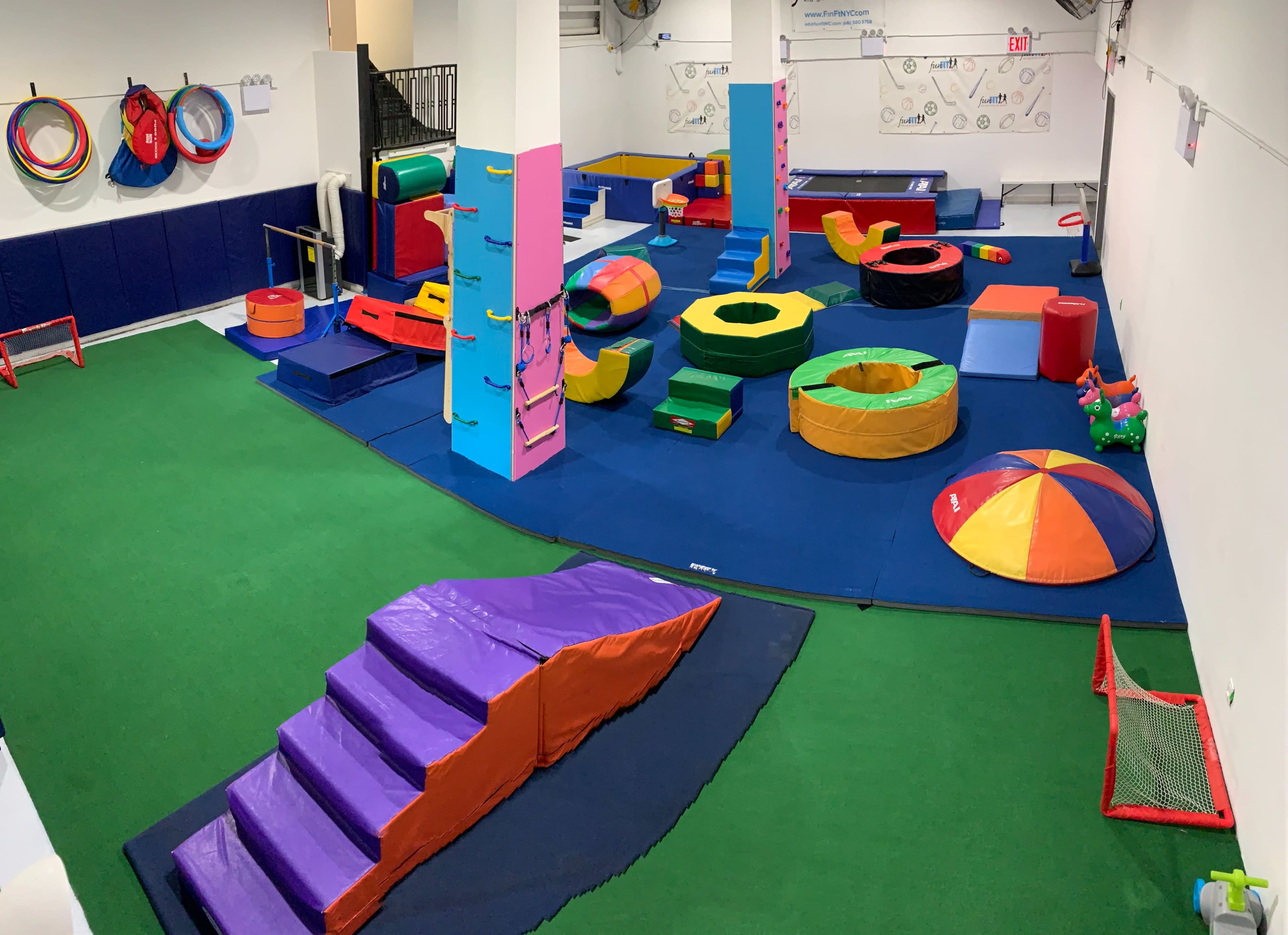 The image shows an indoor play area filled with colorful climbing structures and soft play equipment on a green carpeted floor.