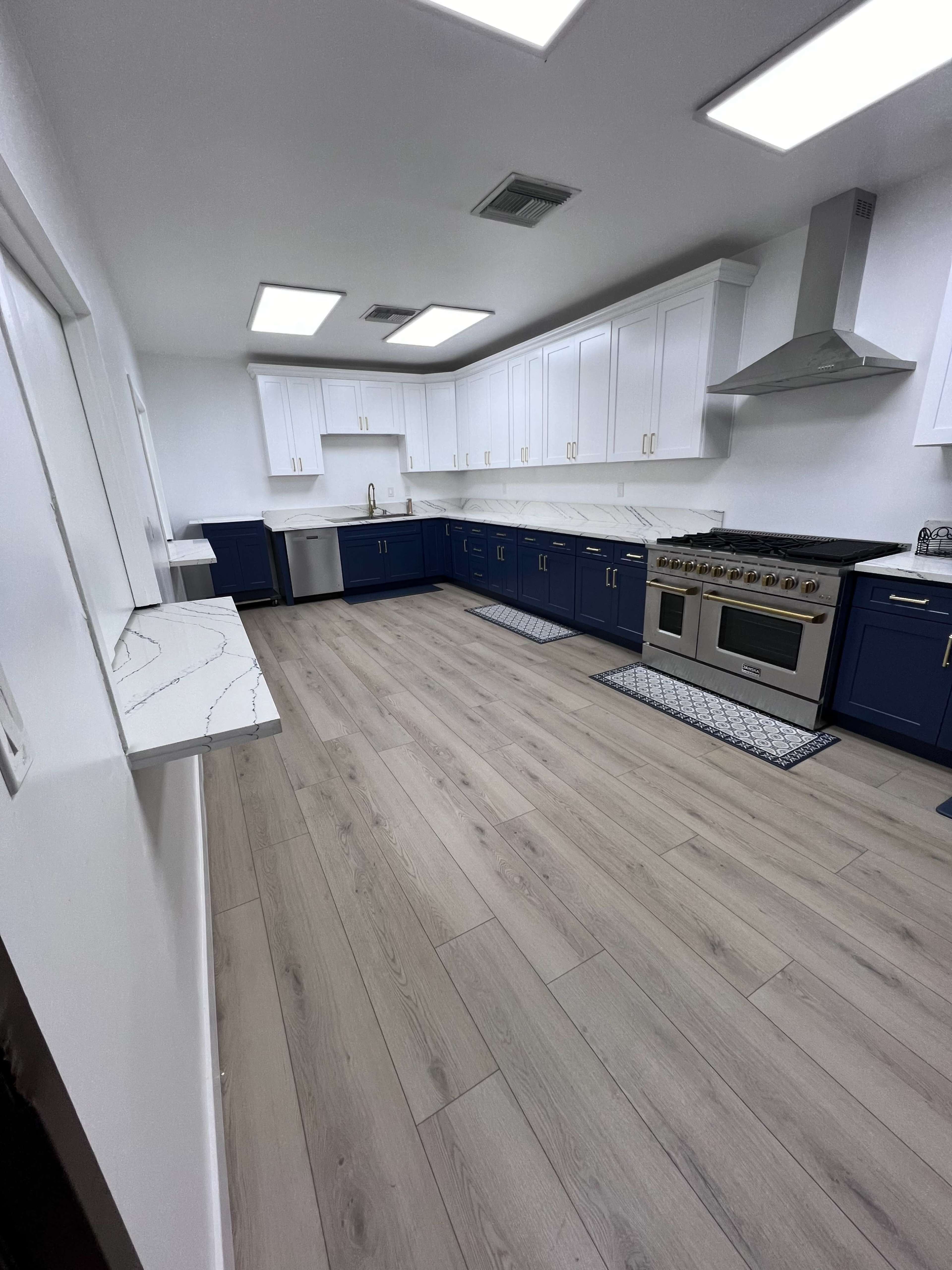 The image shows a modern kitchen with blue and white cabinetry, a large stainless steel stove, and light wood flooring.