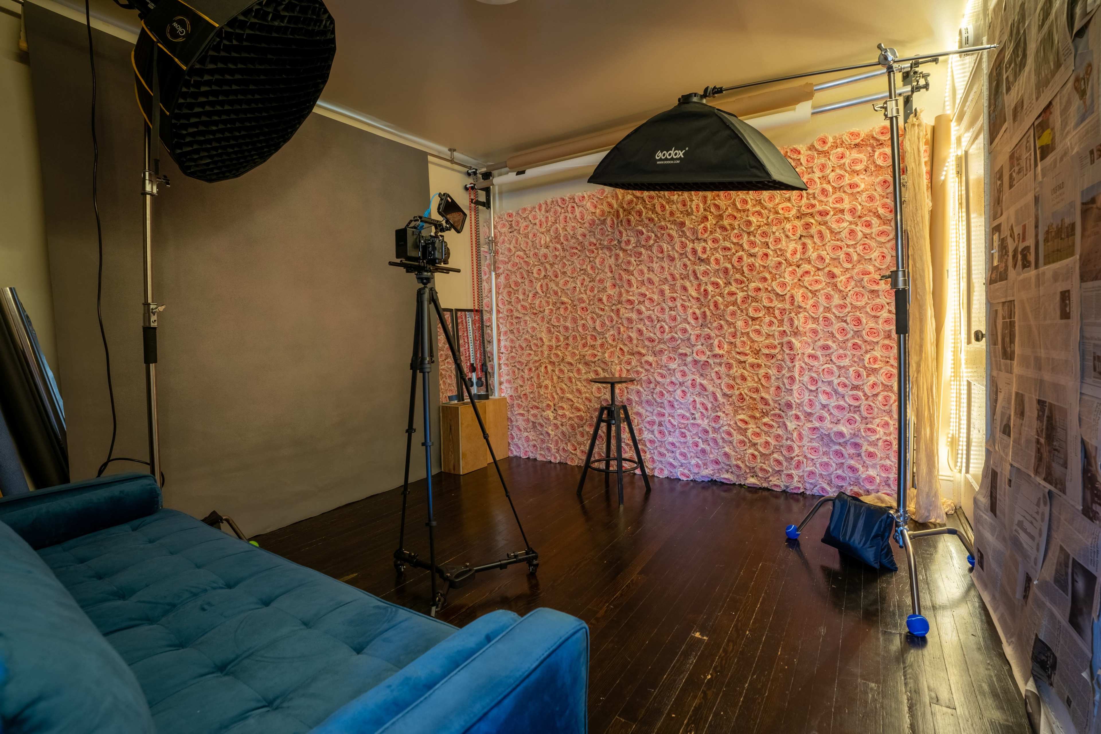 A photography studio with a blue couch, a backdrop covered in patterned fabric, lighting equipment, and a camera on a tripod.