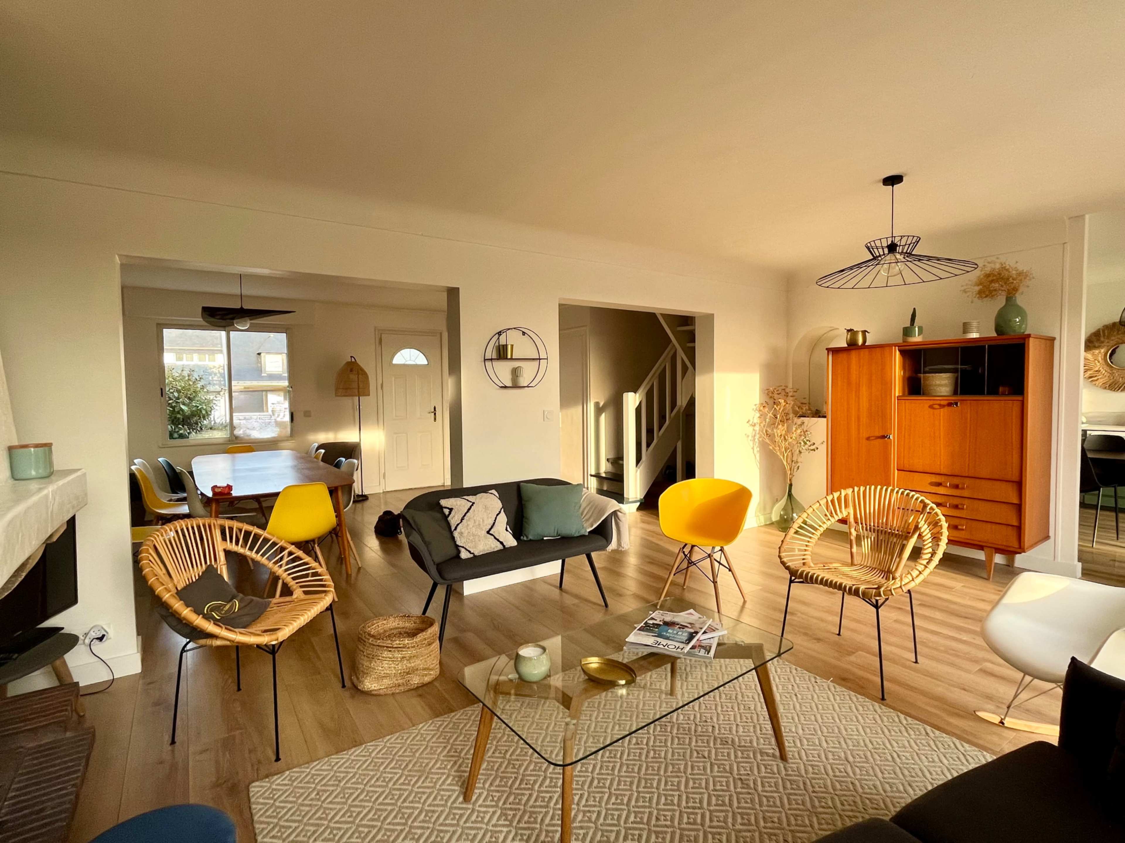 The image shows a modern living room with a mix of seating options, including a black sofa, colorful chairs, and a wooden cabinet, all illuminated by natural light.