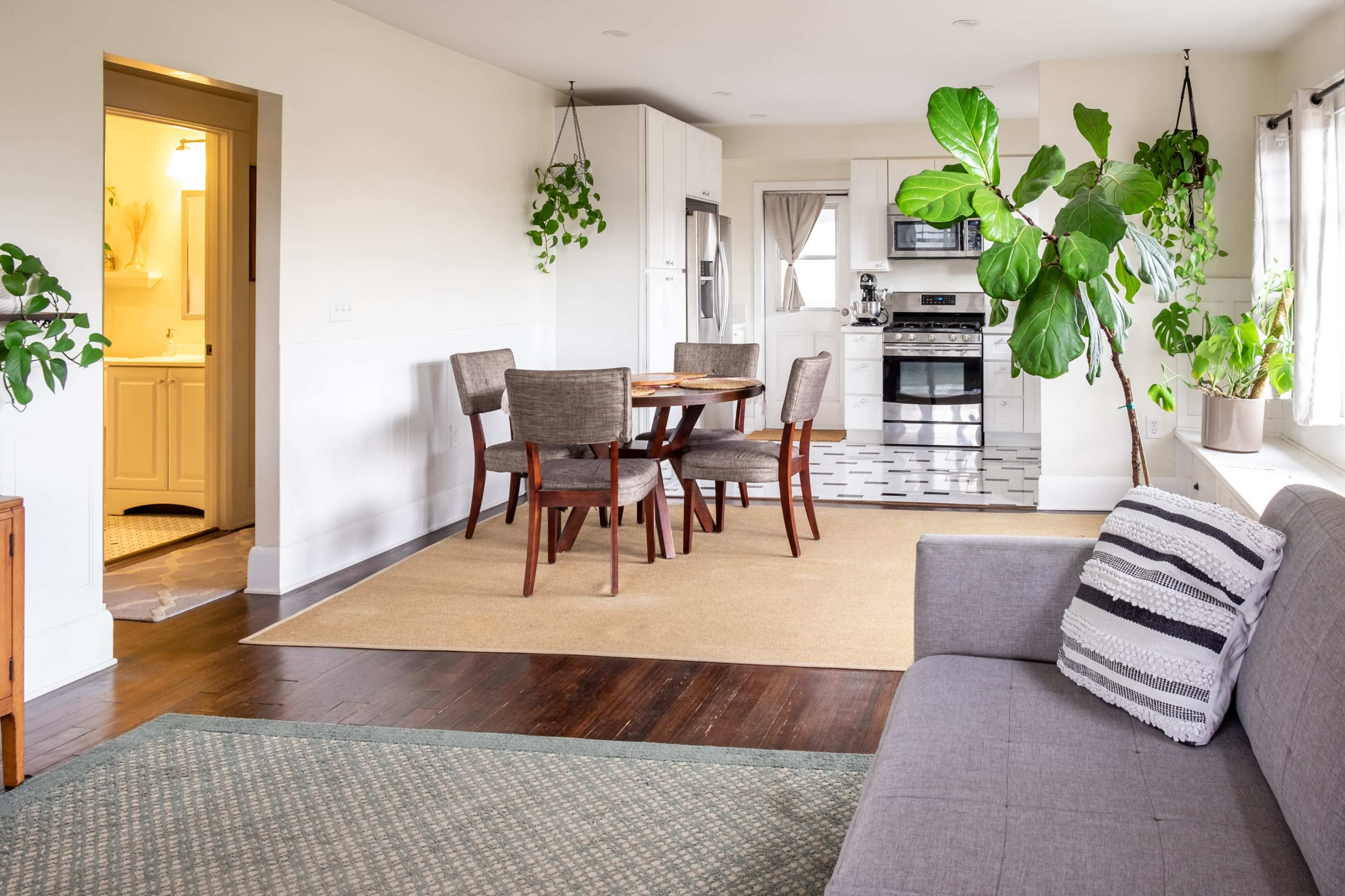 A bright, open-concept living space featuring a dining area with a round table and four chairs, a gray sofa, and a kitchen equipped with modern appliances.