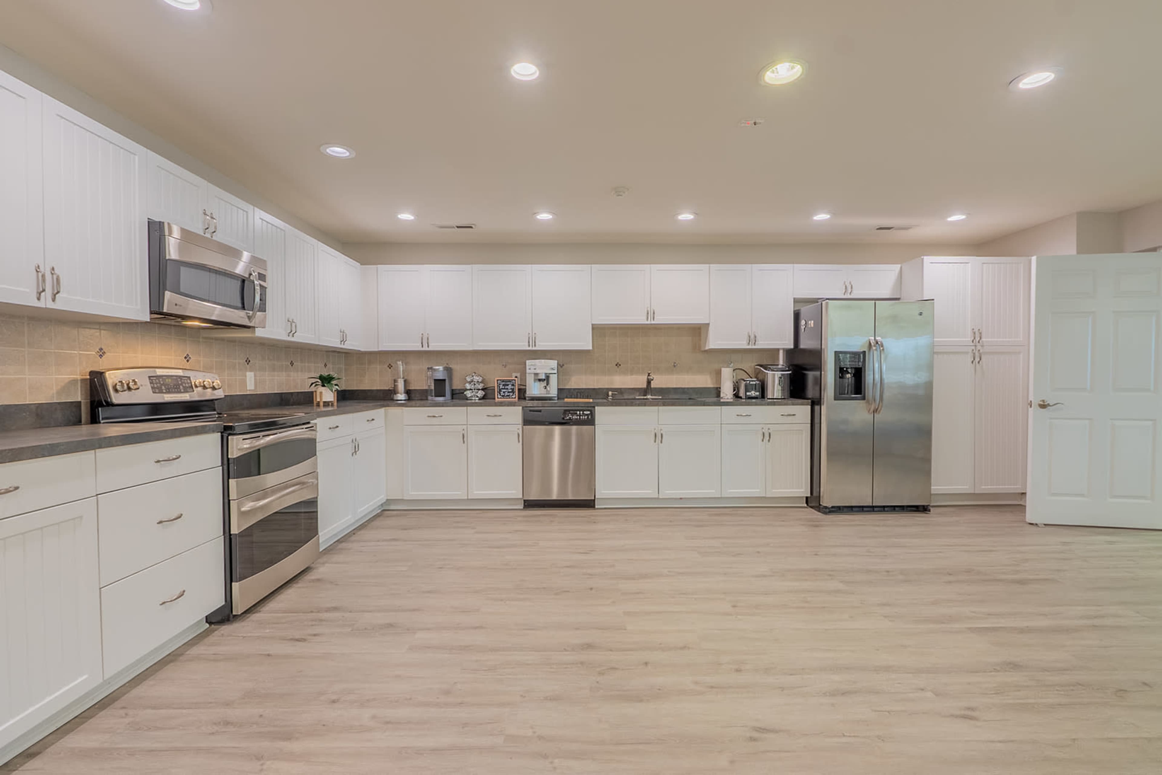 A modern kitchen features white cabinetry, stainless steel appliances, and a light wood floor.