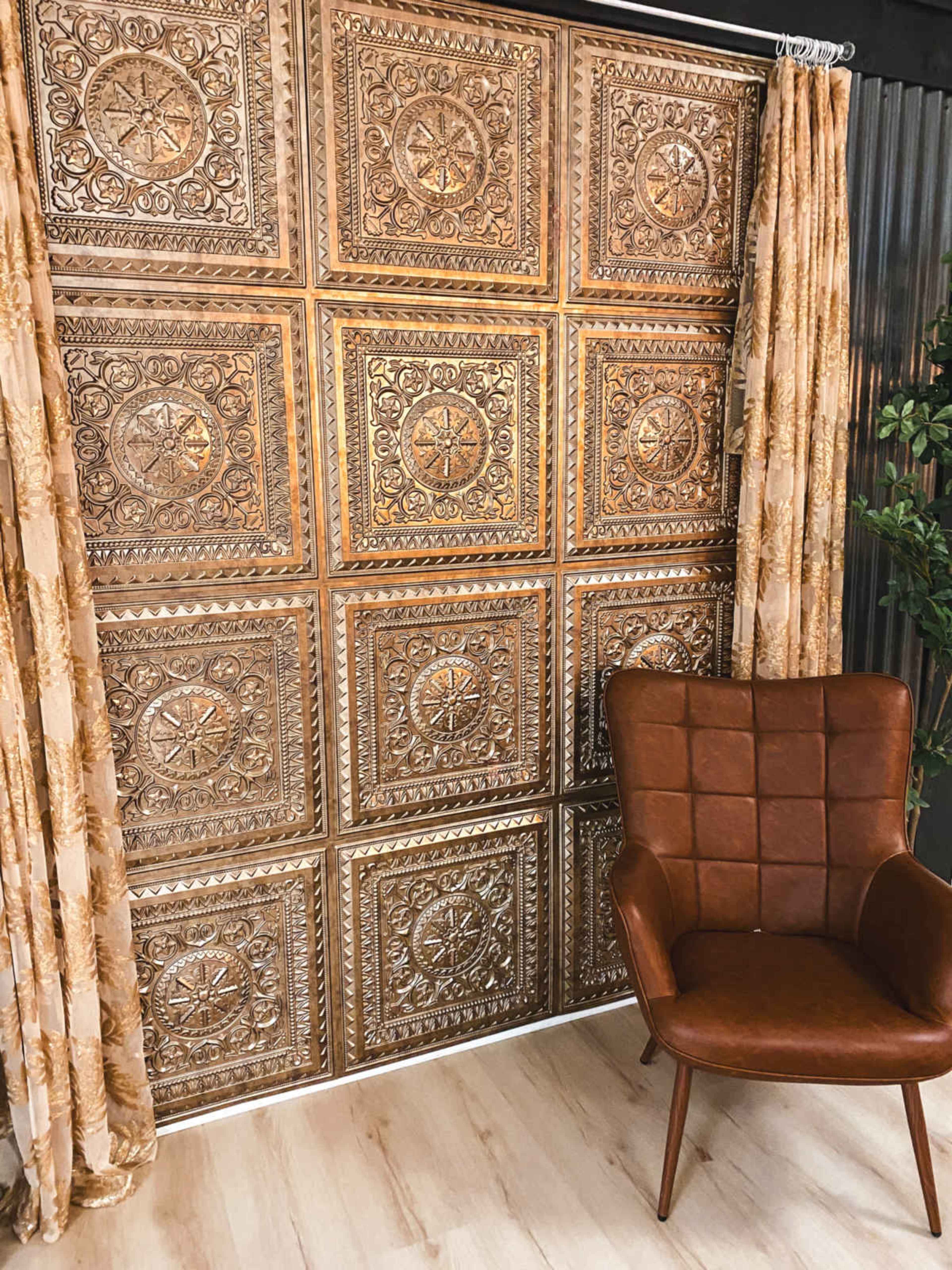 The image shows a textured wall with ornate golden panels behind a brown leather armchair and patterned curtains.
