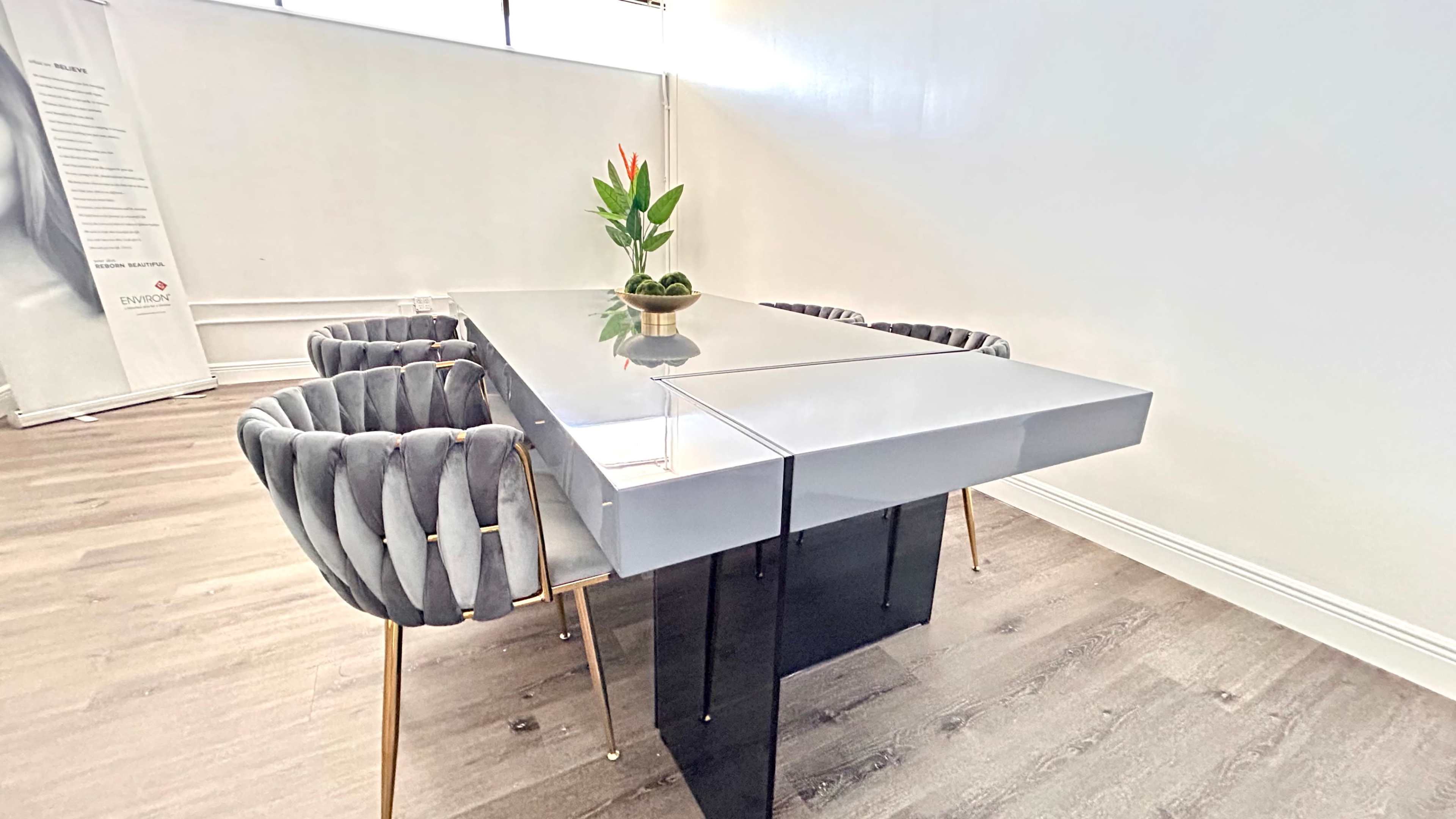 A modern conference table with a shiny surface is surrounded by four gray upholstered chairs, and a small plant is placed in the center.