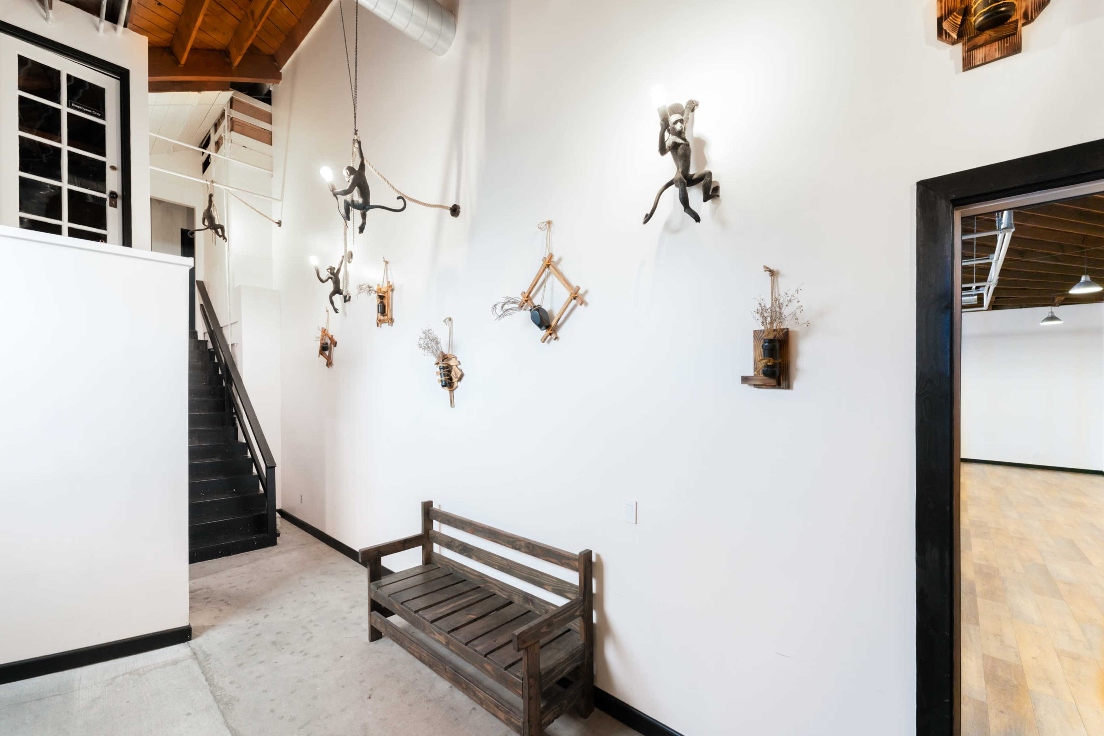 A minimalist entryway featuring a wooden bench against a white wall adorned with decorative wall art and a staircase leading to a lofted area.