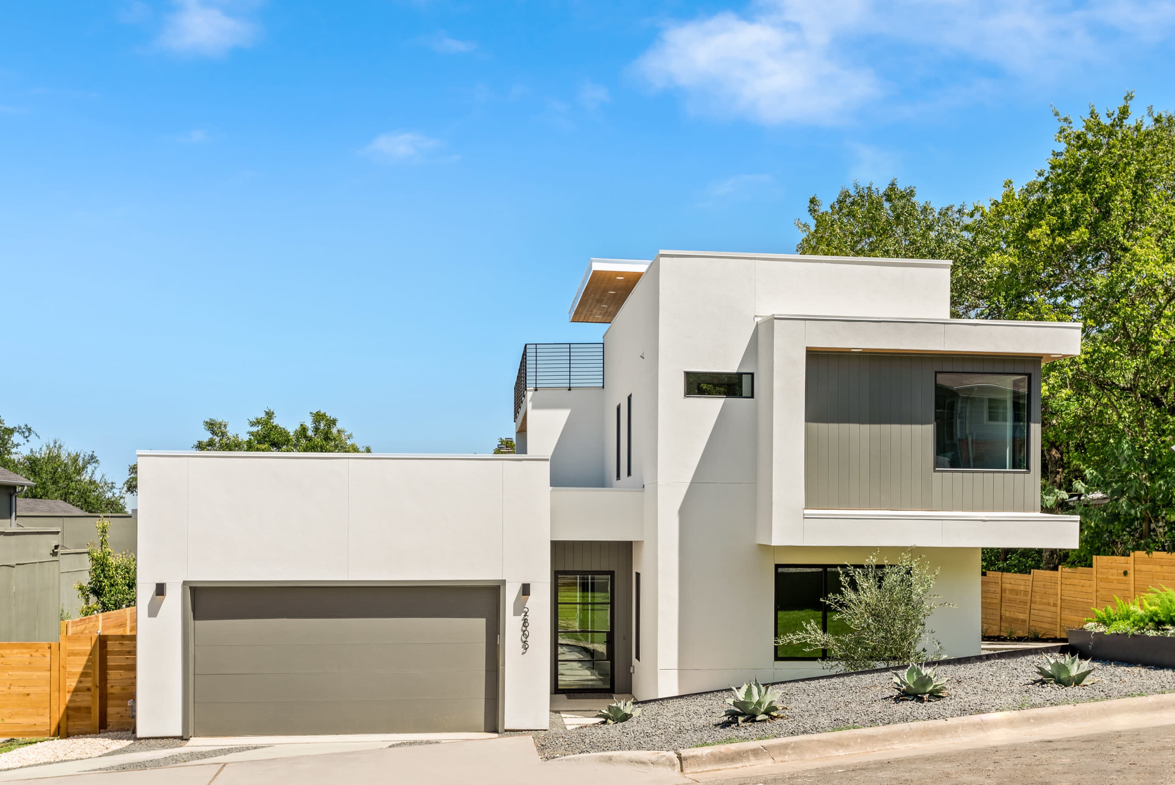 The image shows a modern, two-story white house with large windows, a garage, and a landscaped yard featuring succulents.