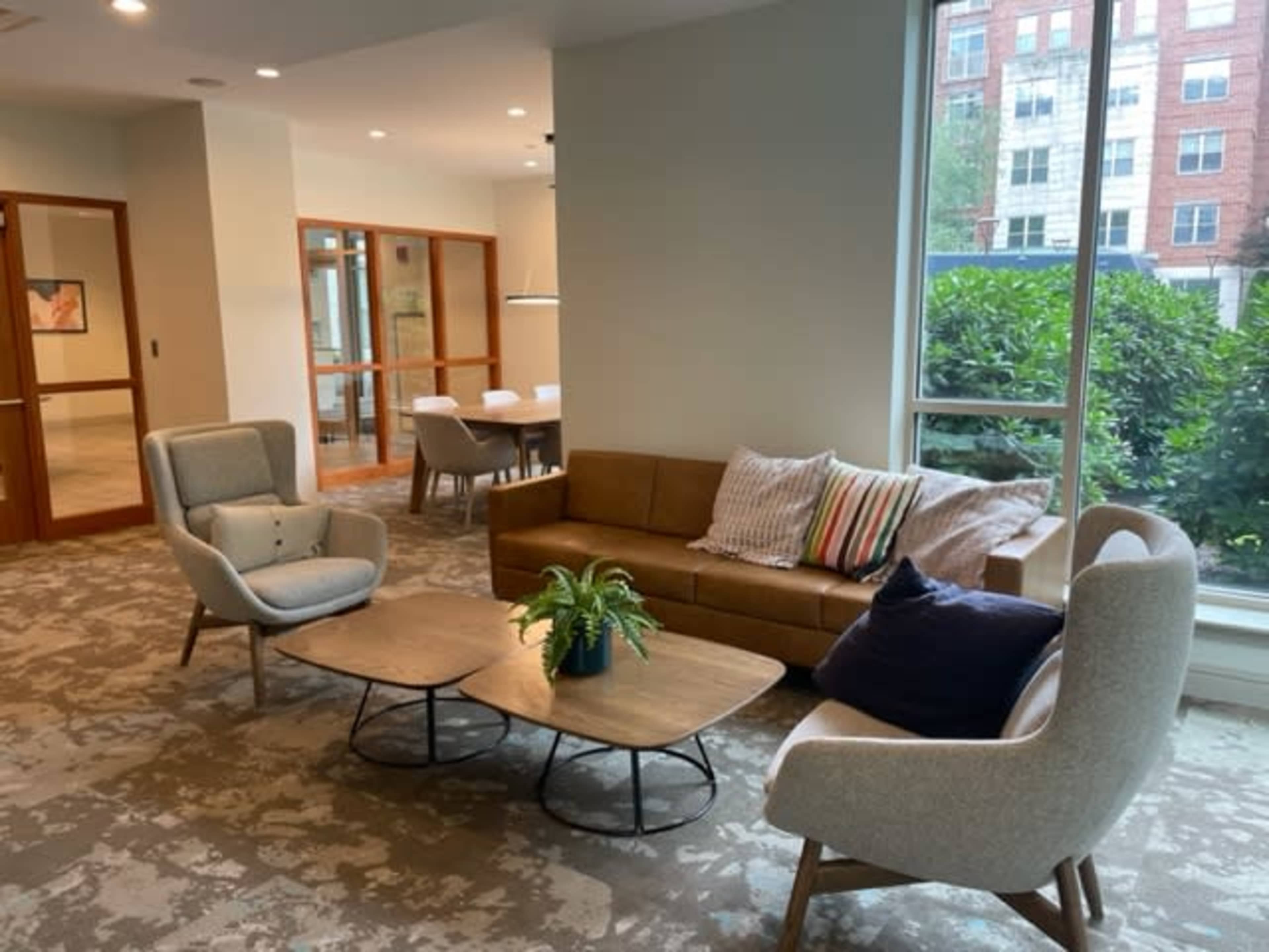 A cozy lounge area with a brown sofa, two armchairs, and a coffee table surrounded by large windows.