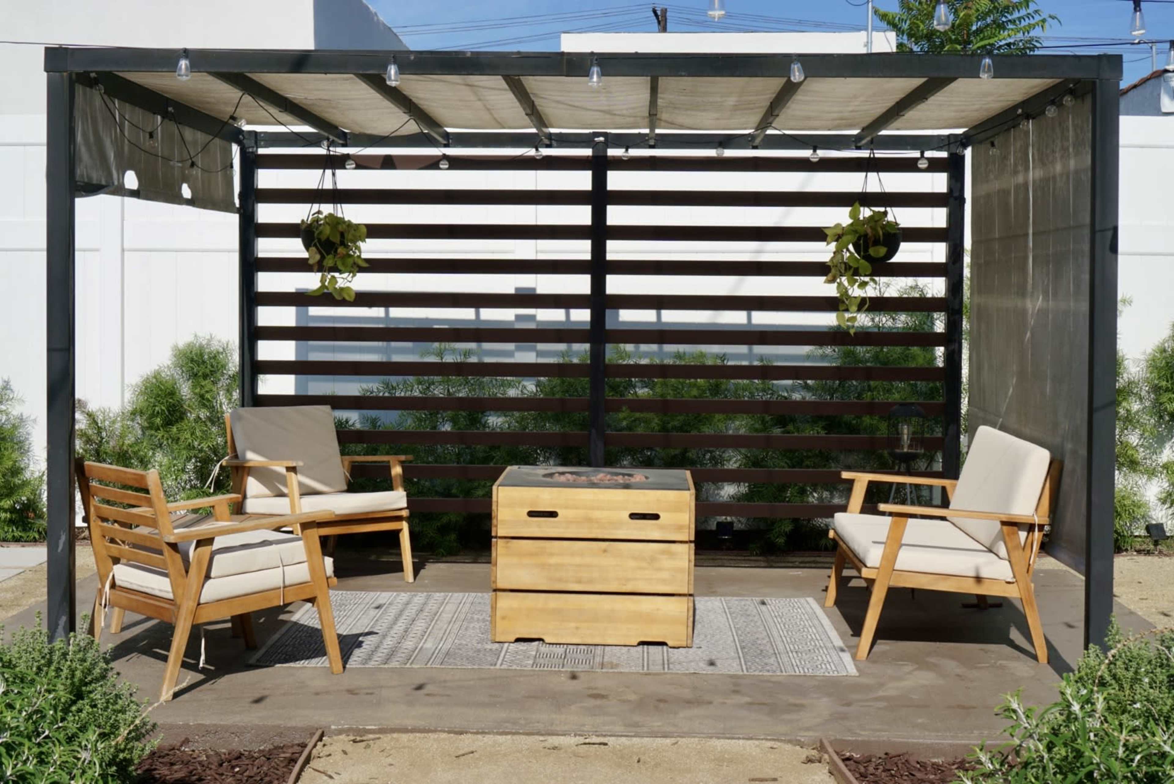 A covered outdoor seating area with two wooden chairs, a central table, and hanging plants.