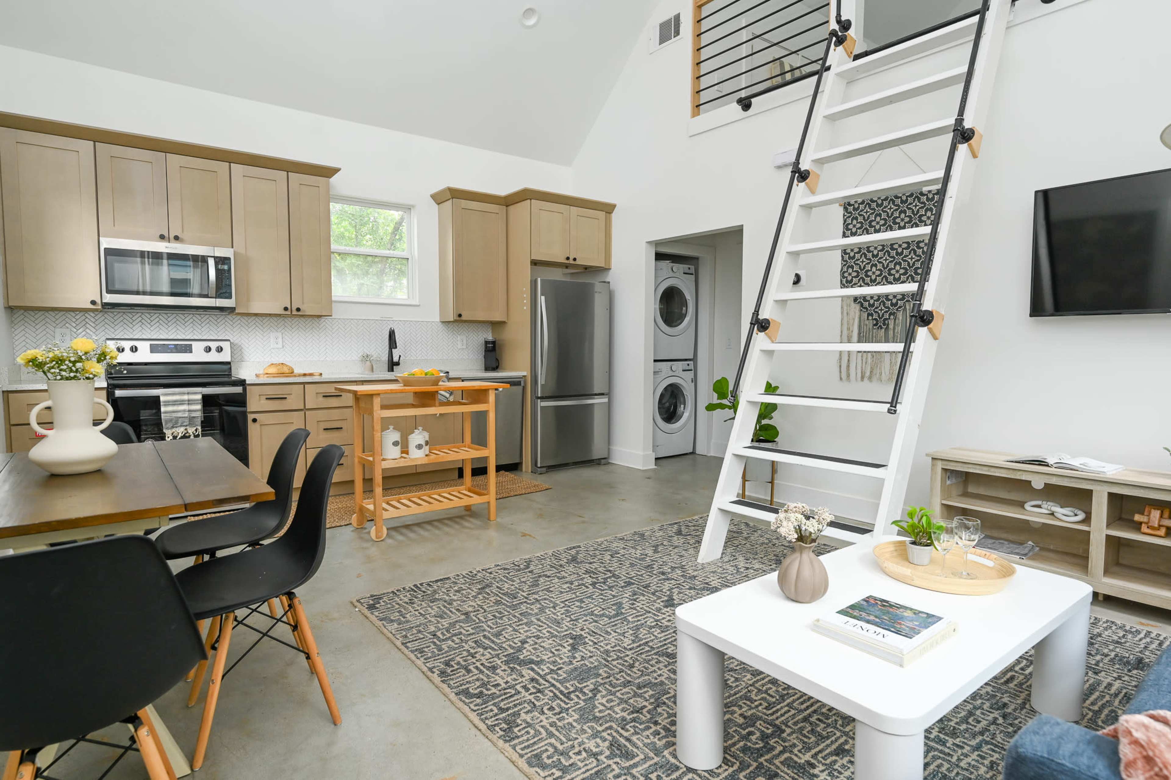 The image shows a modern, open-concept kitchen and dining area with a staircase leading to a loft space.