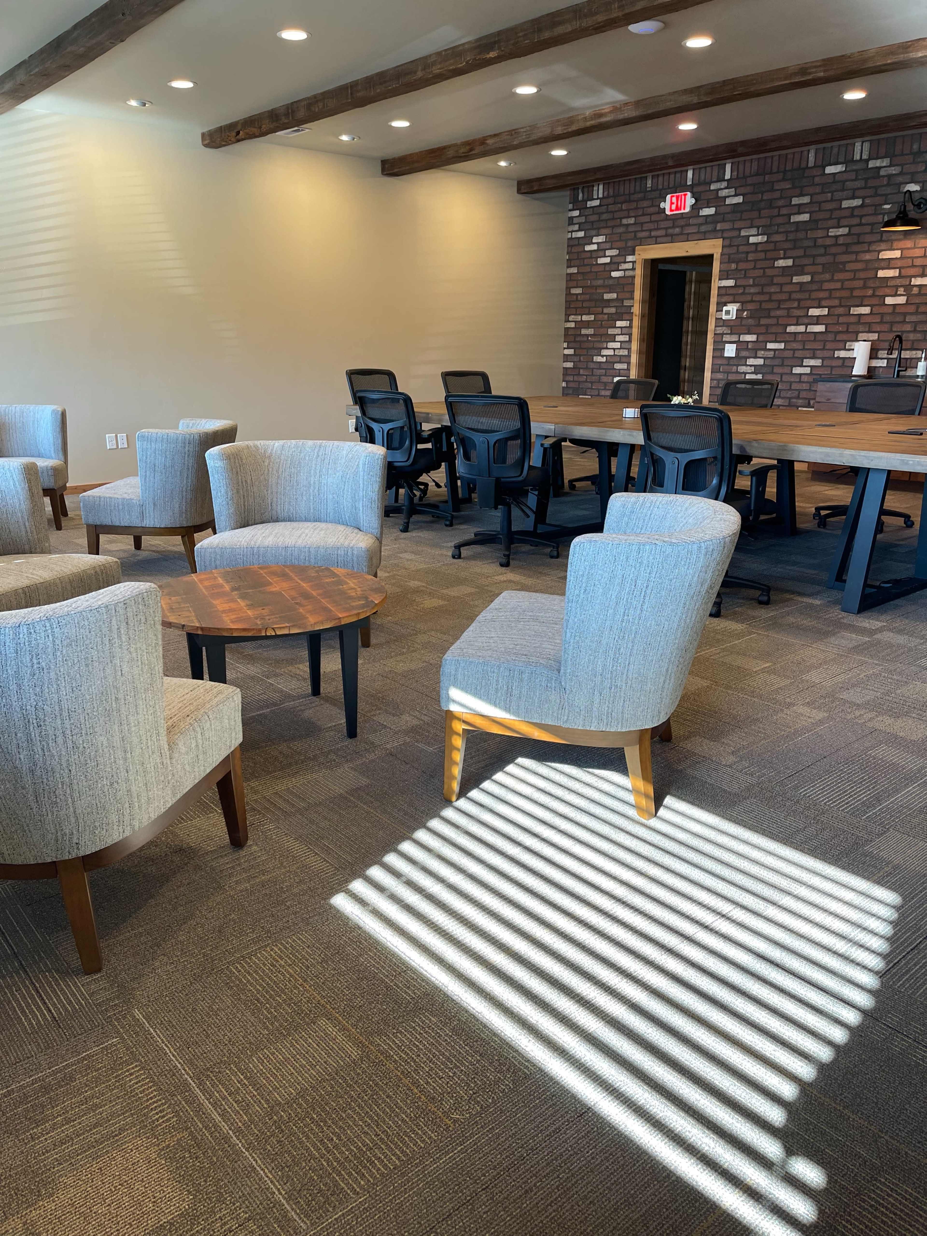 A modern meeting room with several chairs and a table arranged near a brick wall and a large conference table set for a meeting.