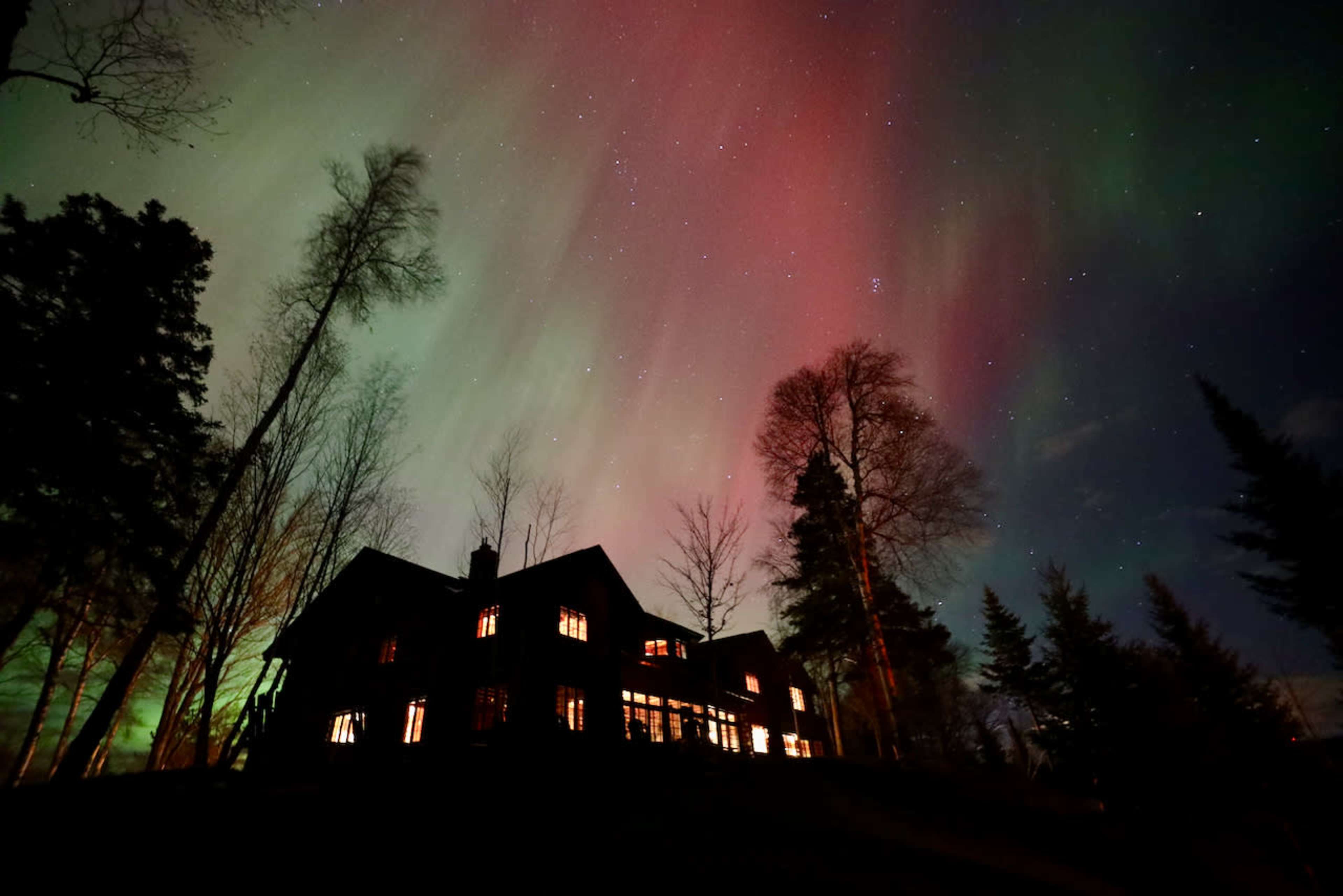 A dark silhouette of a house stands against a vibrant sky illuminated by the northern lights.