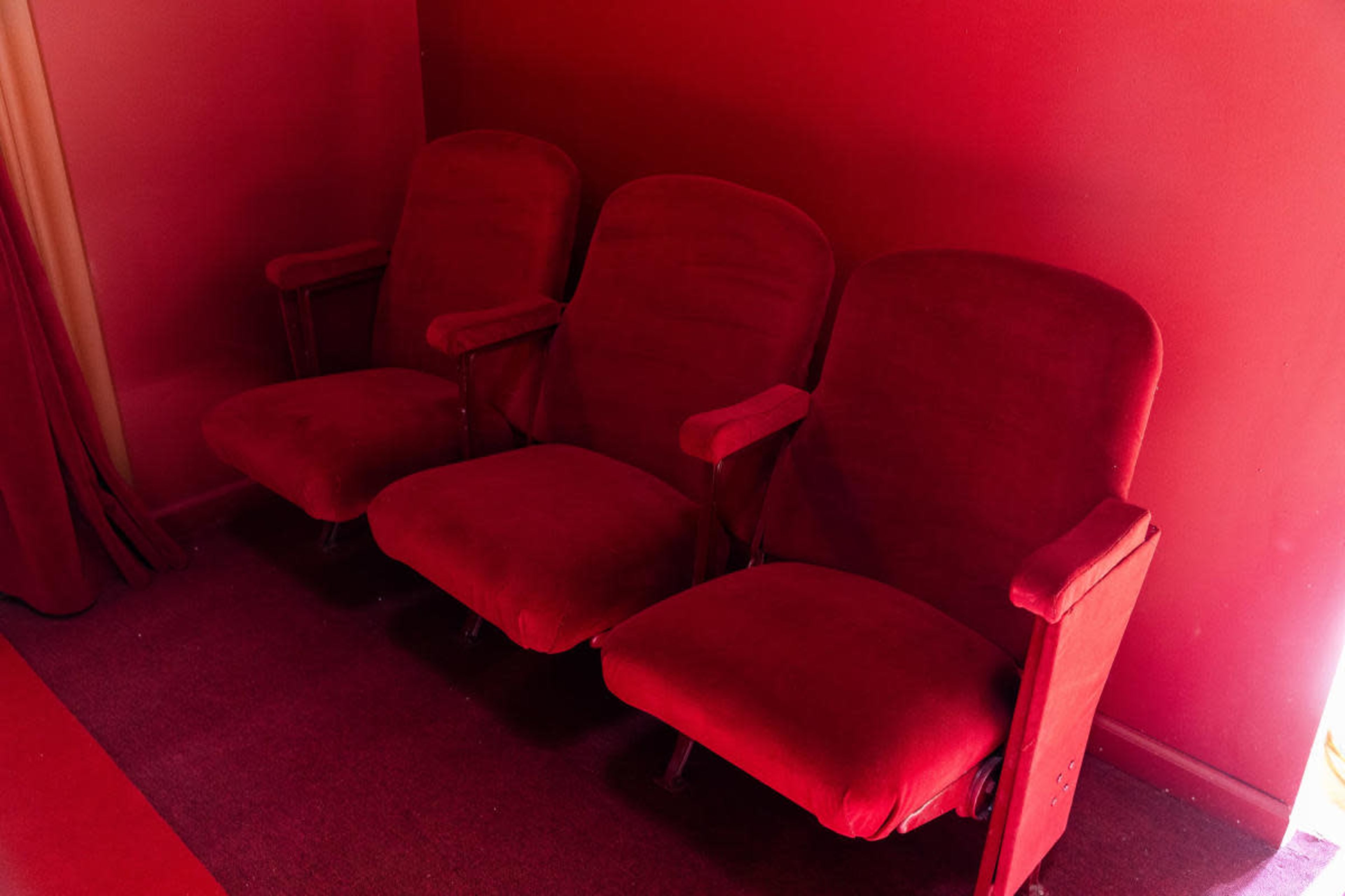The image shows three red upholstered theater seats against a matching red wall.