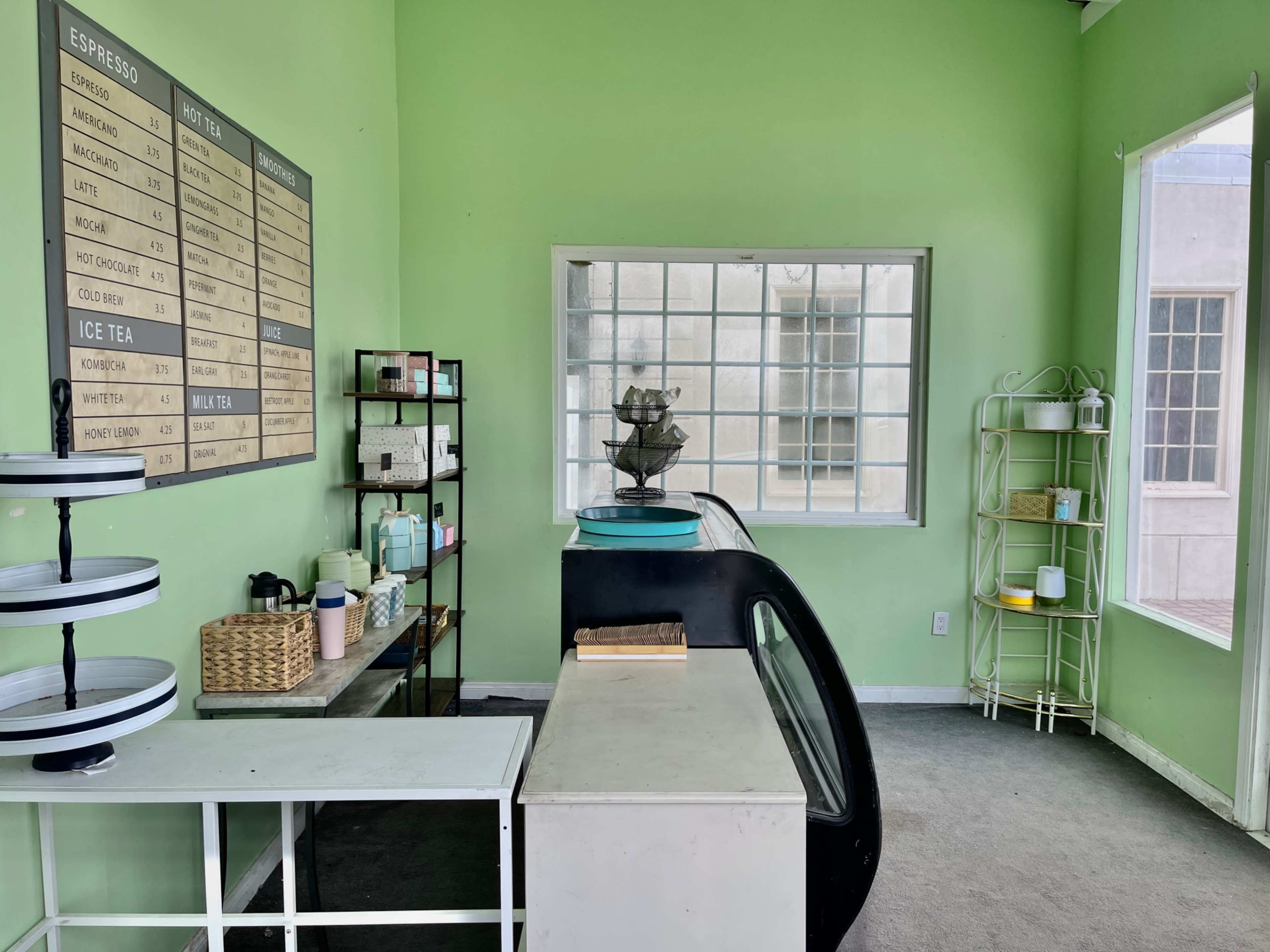 A brightly colored green café interior with a display counter, menu board, and a variety of shelves filled with products.
