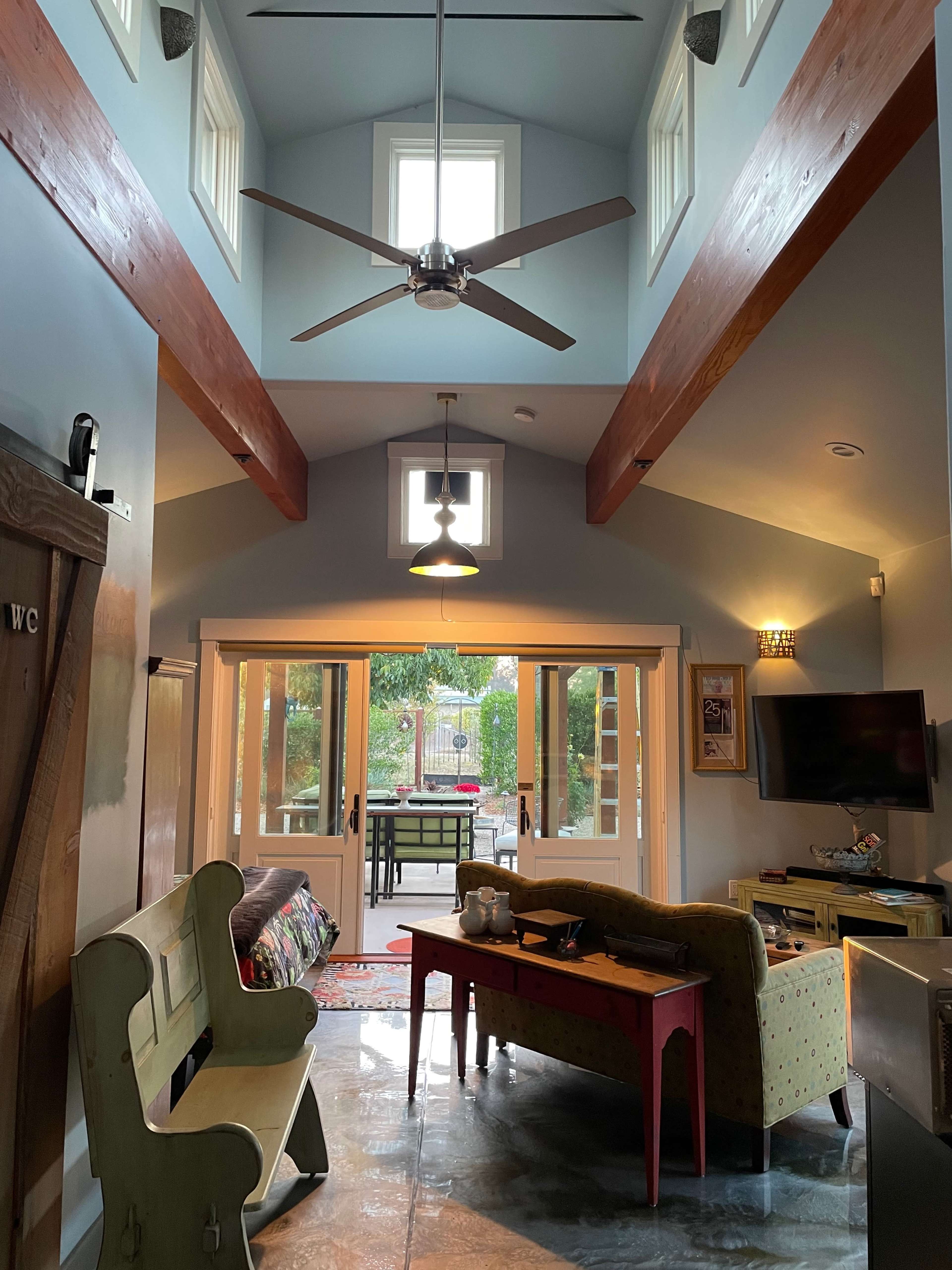 A spacious living area with high ceilings, large windows, and a view of an outdoor patio through glass doors.