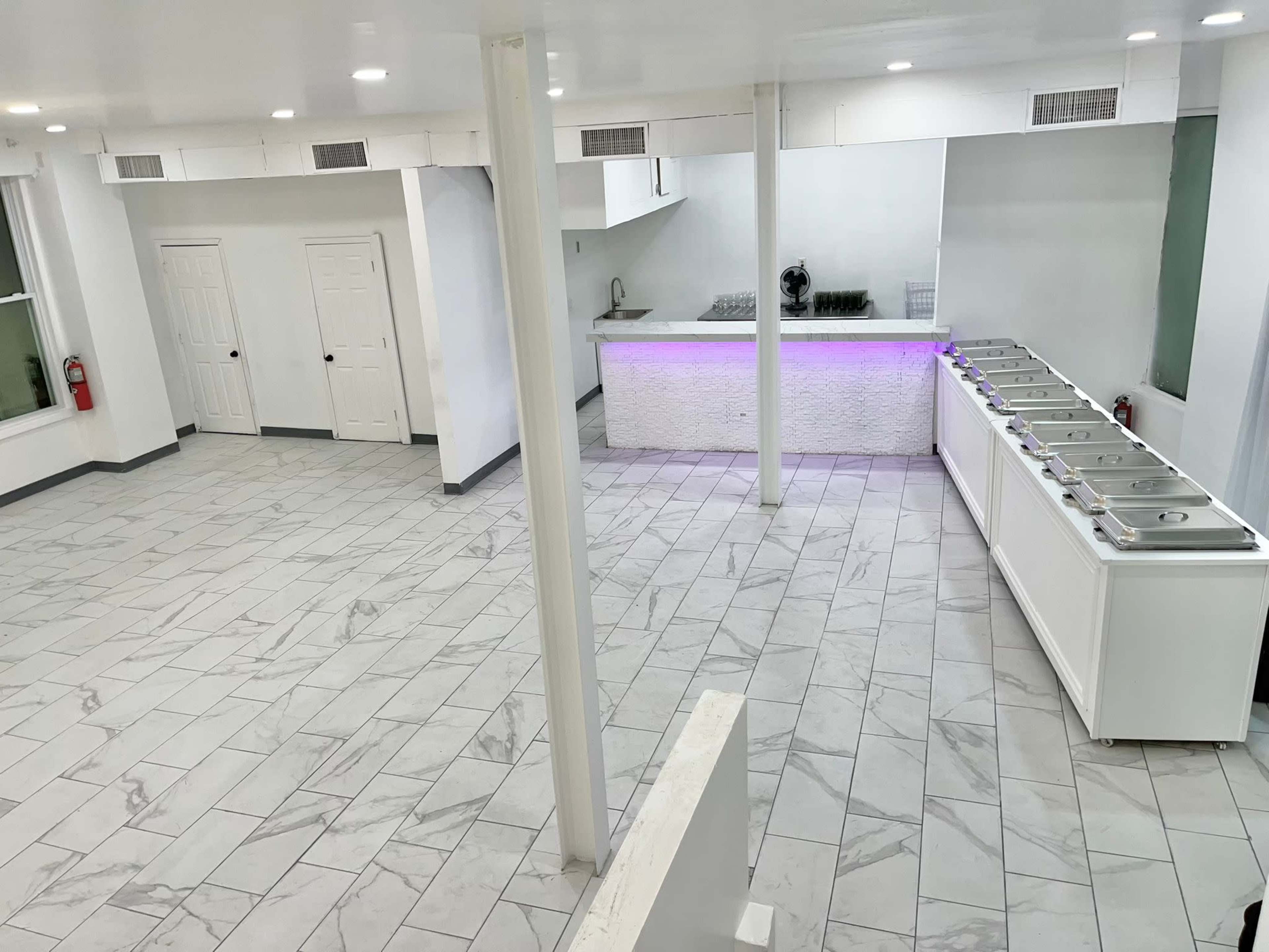 An empty commercial space with a tiled floor, white walls, and a serving counter with multiple ice cream tubs.