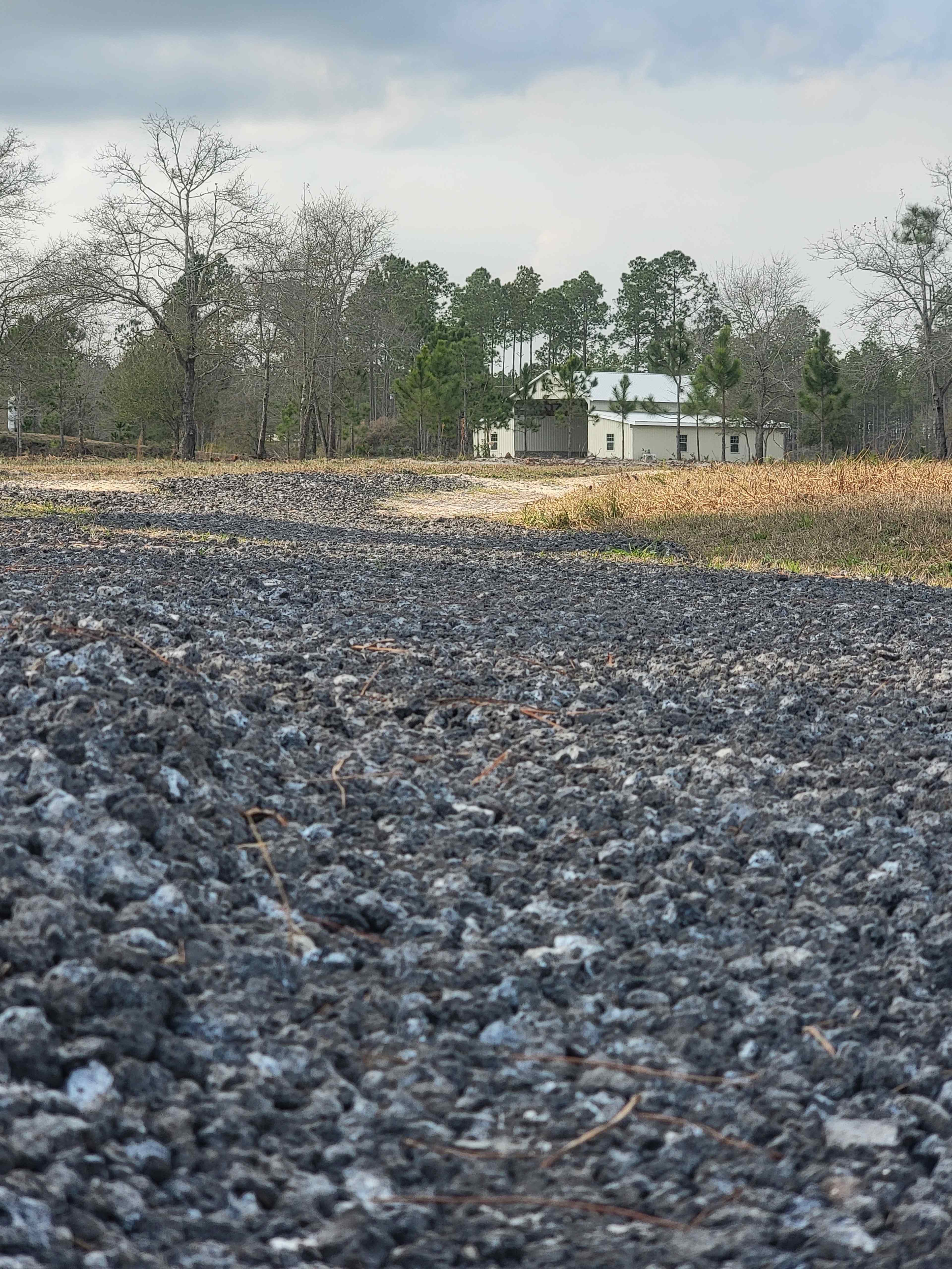 A gravel path leading toward a white building surrounded by trees in a rural area.