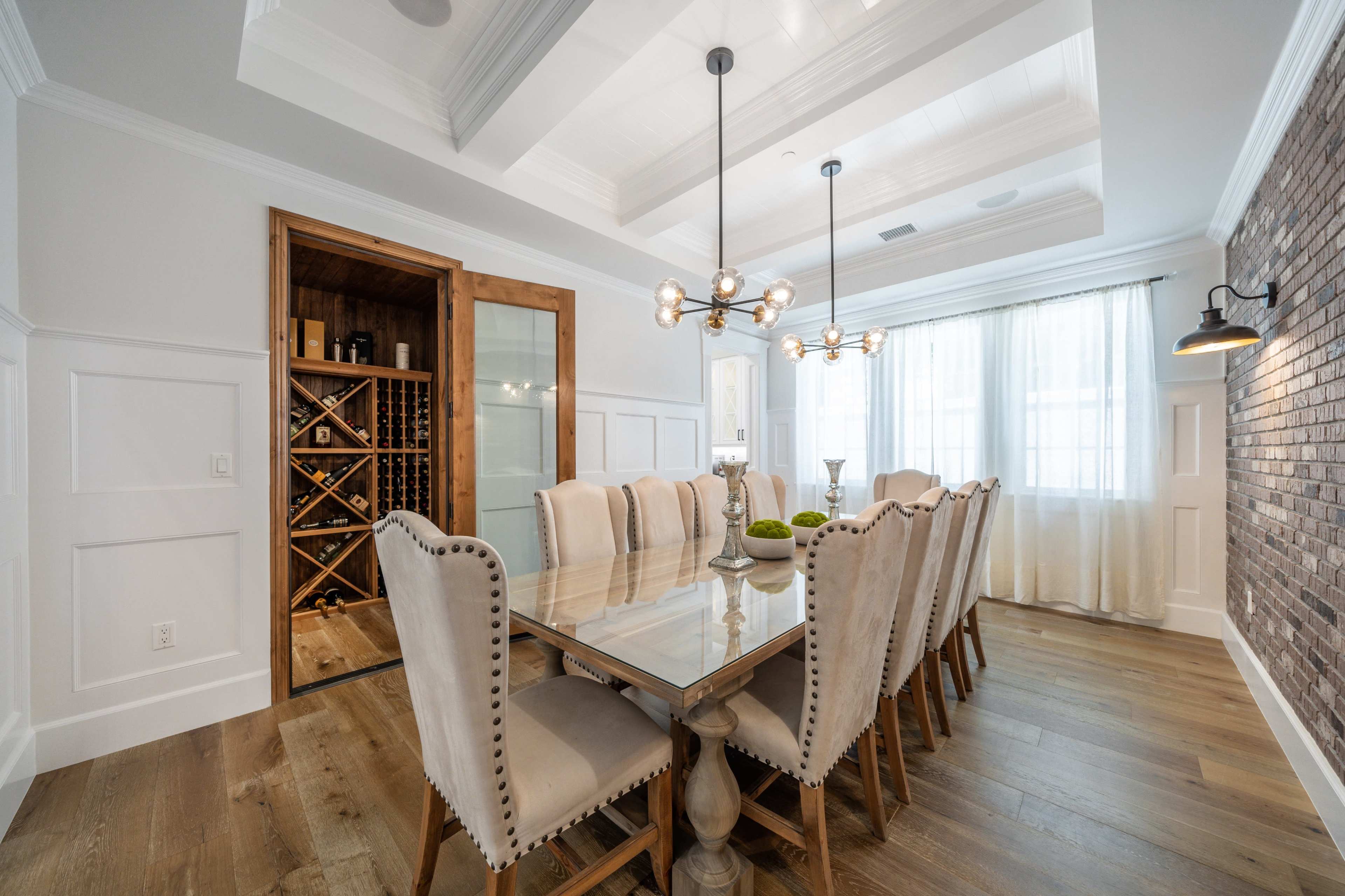 A spacious dining room features a long table surrounded by upholstered chairs, with a wine cellar accessible through a wooden door.