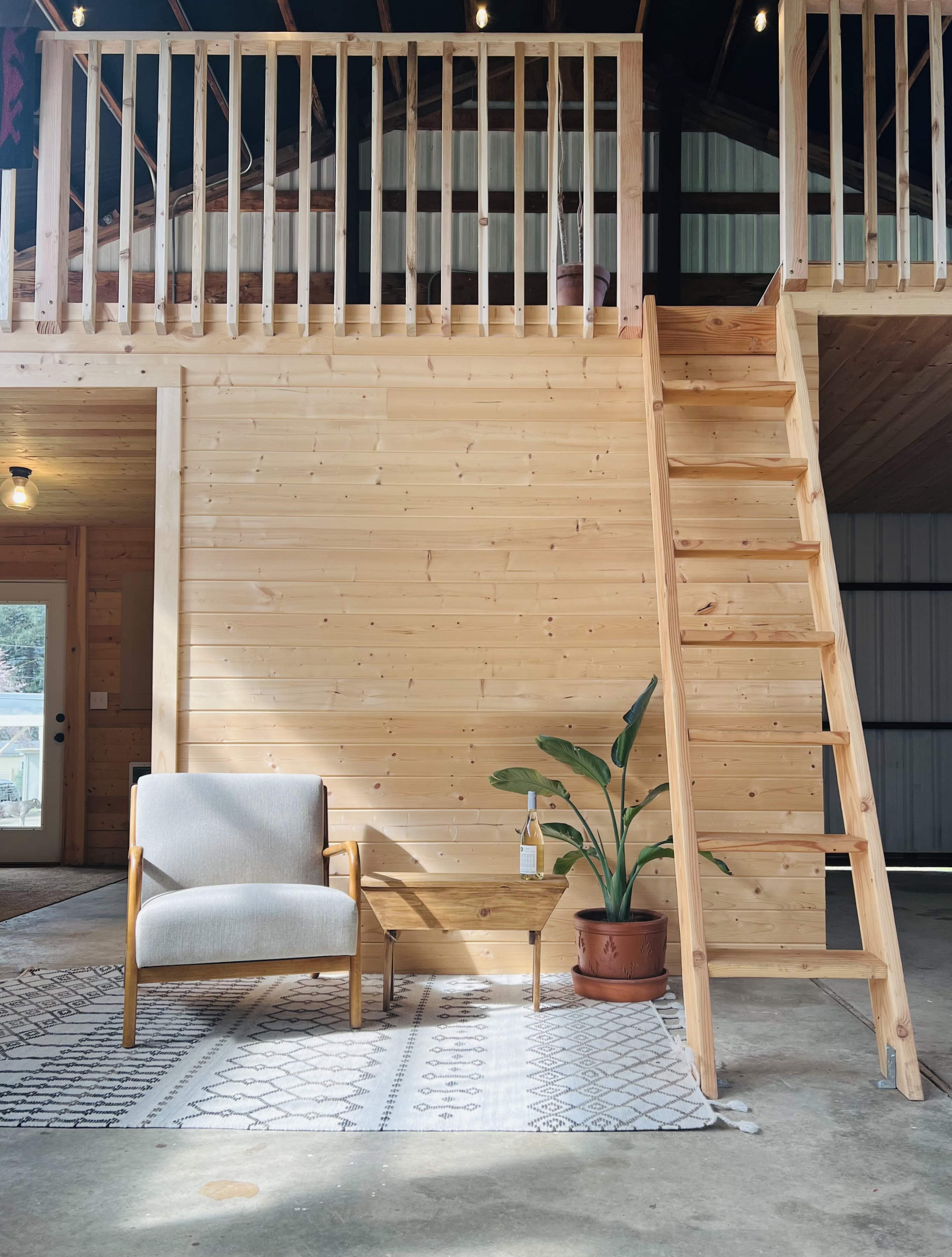 A cozy sitting area features a wooden chair and table next to a potted plant, with a staircase leading to a higher level in a wooden interior space.