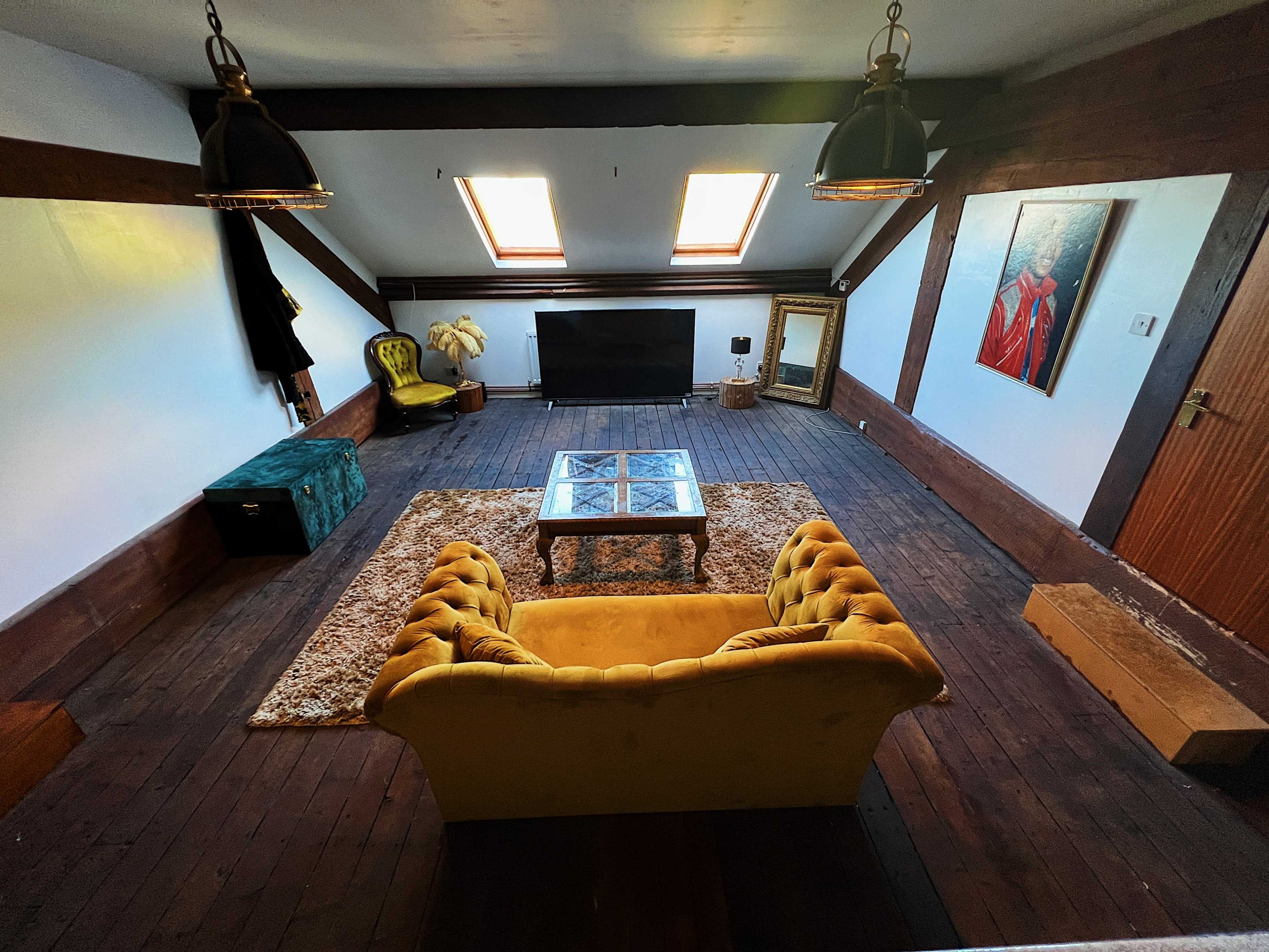 A spacious living area with a yellow couch, a glass coffee table, a television, and a couple of skylights illuminating the wooden floor.