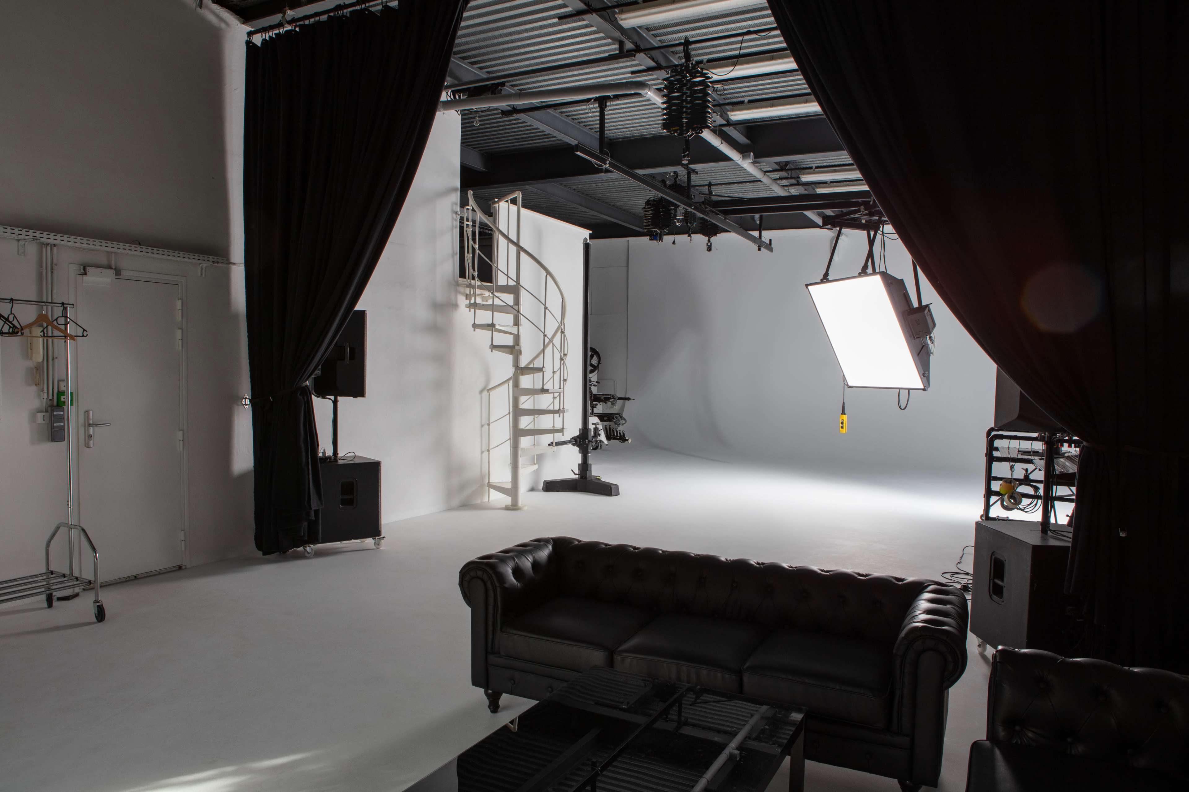 A photography studio with a spiral staircase, lighting equipment, and a black couch in the foreground.